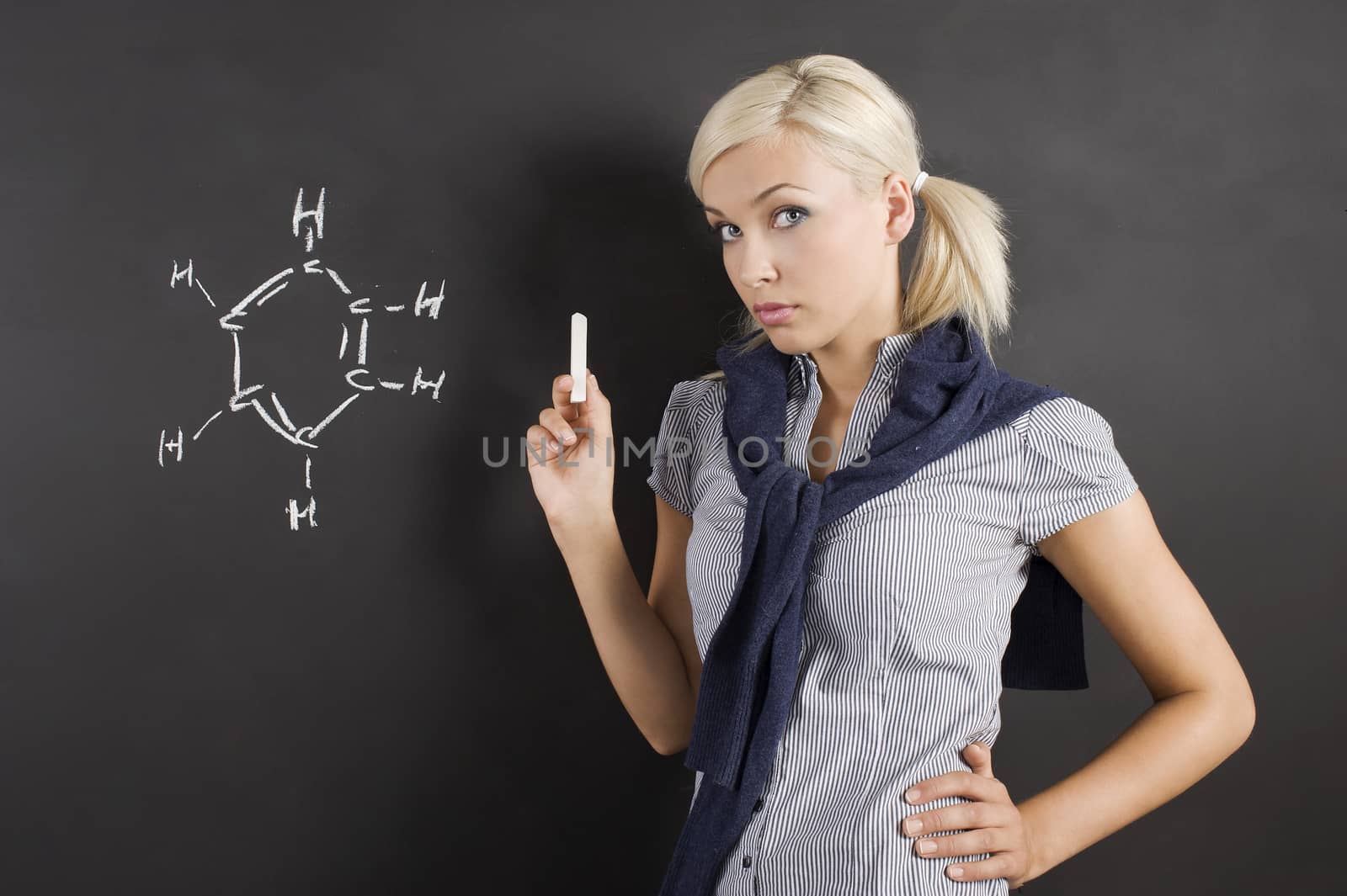 pretty young college student near a blackboard with a white chalk in hand looking in camera