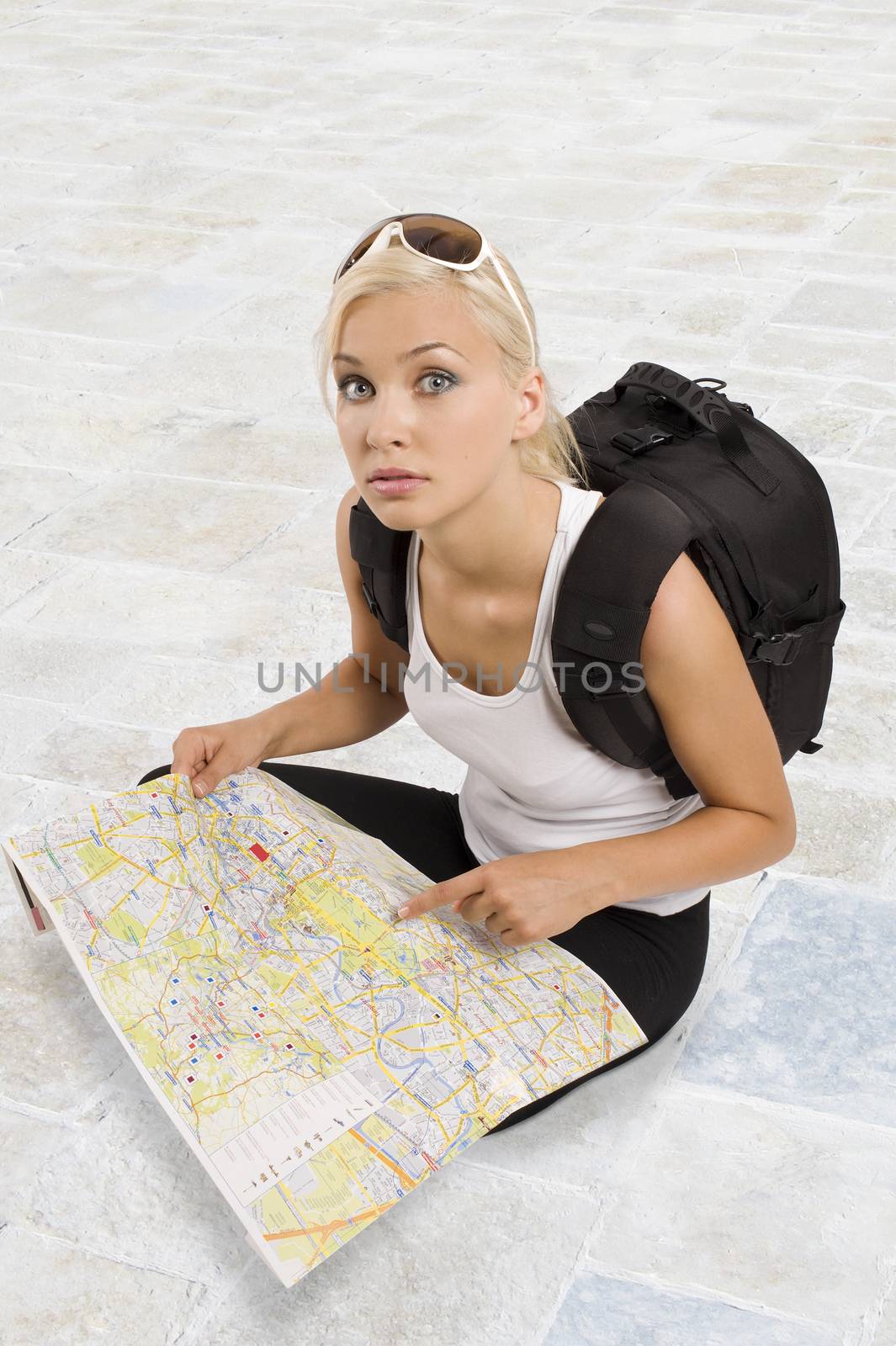 young pretty student girl in vacation with a map sitting down and looking in camera