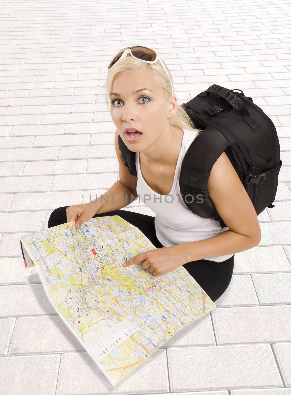 pretty girl in vacation with backpack sitting down with map and looking in camera surprised