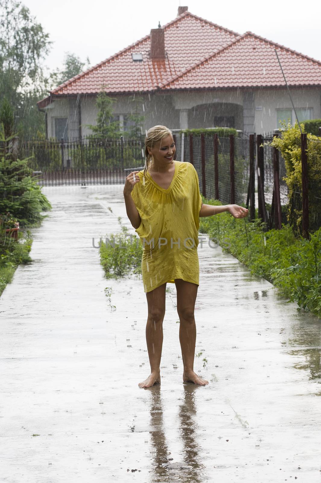 young blond woman in yellow dress under rain falling down outside of home