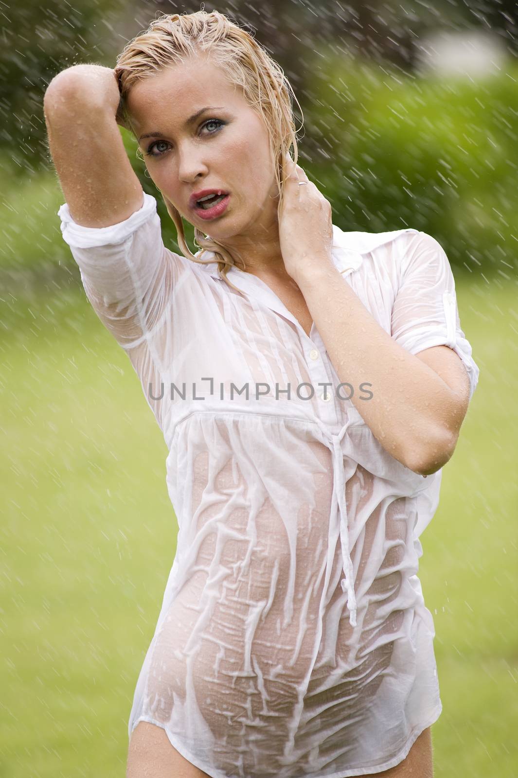 young sexy blond woman otodoor in a garden playing with water and rain with wet dress