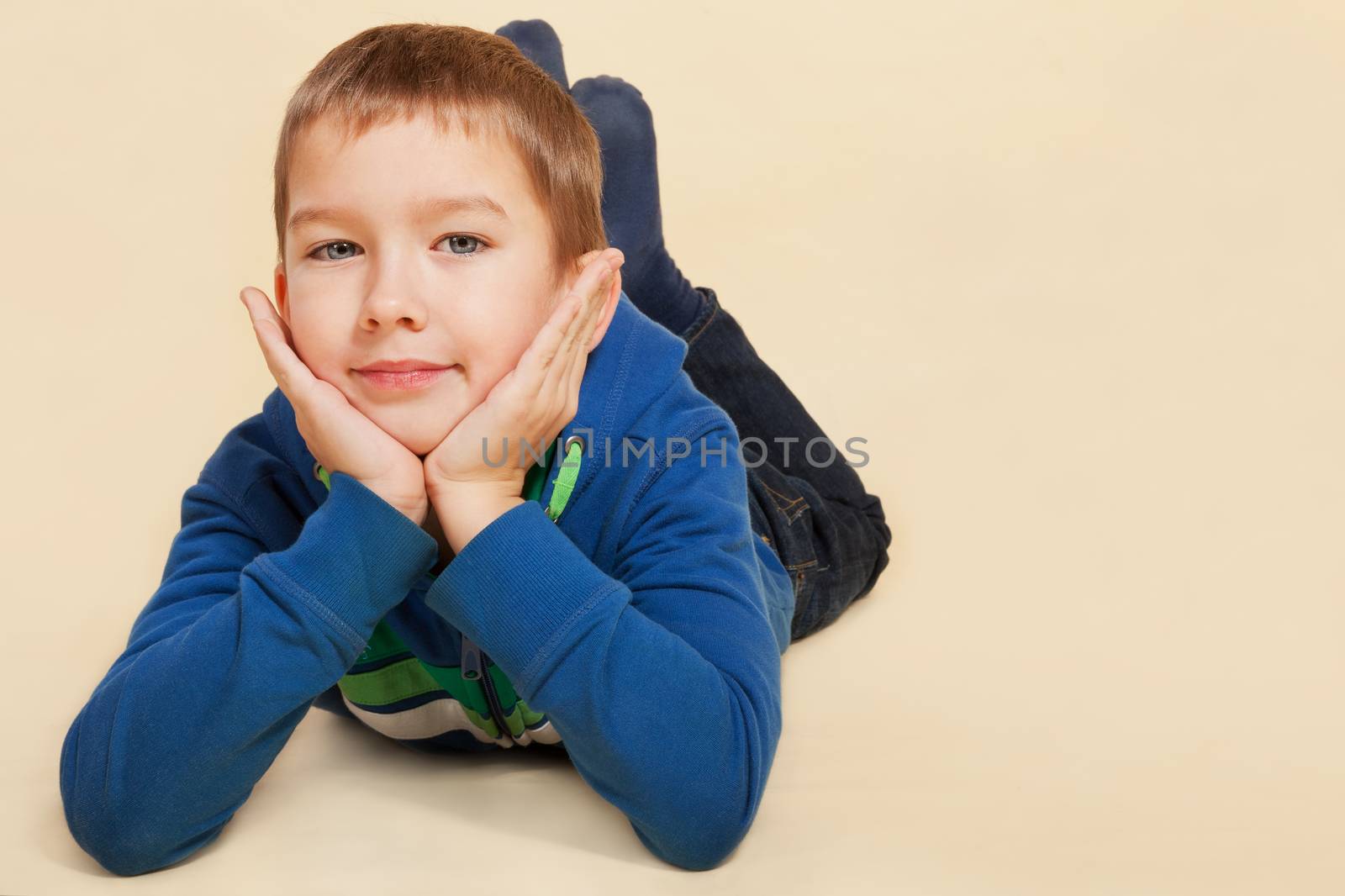 Young boy in casual cloth lying on the ground, hands on chin, smiling and looking into the camera. Youth lifestyle concept.