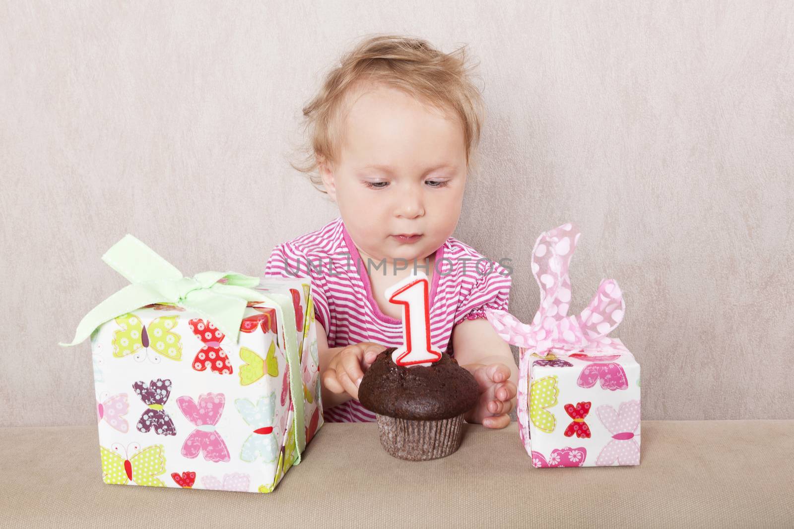 First birthday. Charming caucasian baby girl with presents and birthday cake on beige background. 