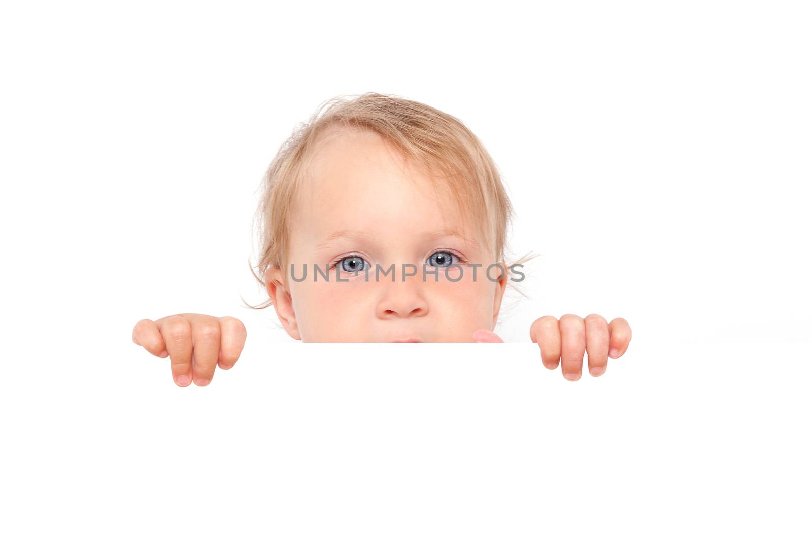 Cute blonde baby girl with big blue eyes looking over white board isolated on white background. Cute curious baby and family concept.