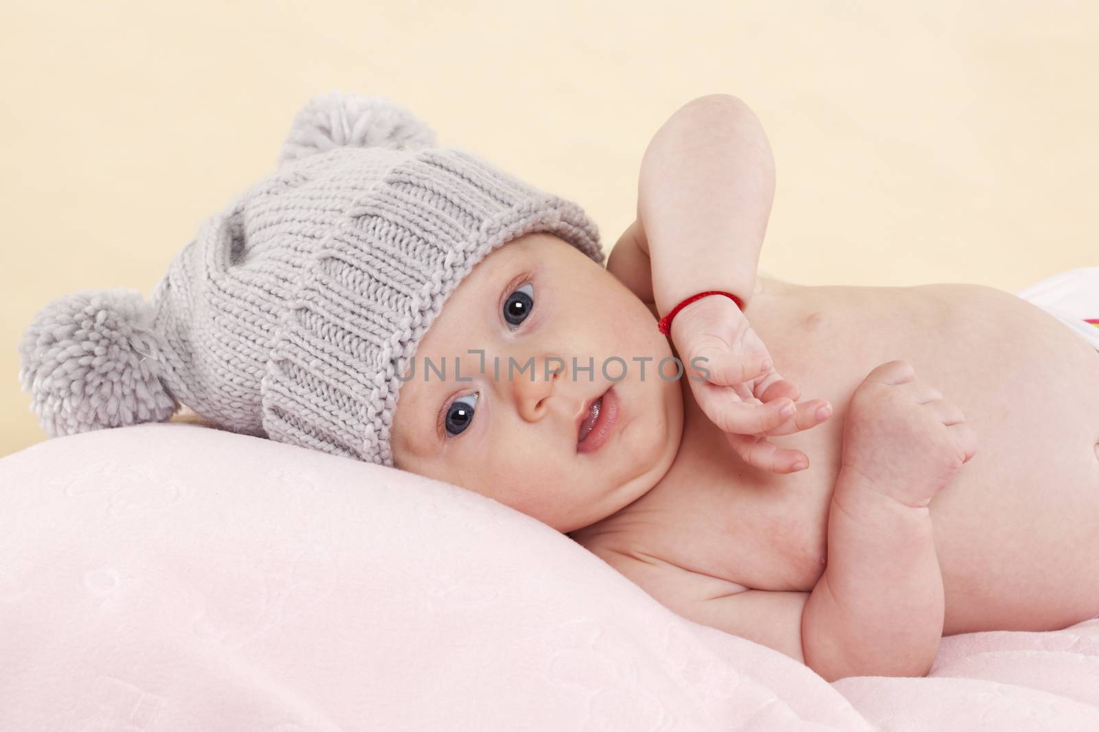Cute naked baby girl with grey hat lying on a blanket and looking into the camera. Beautiful newborn concept.