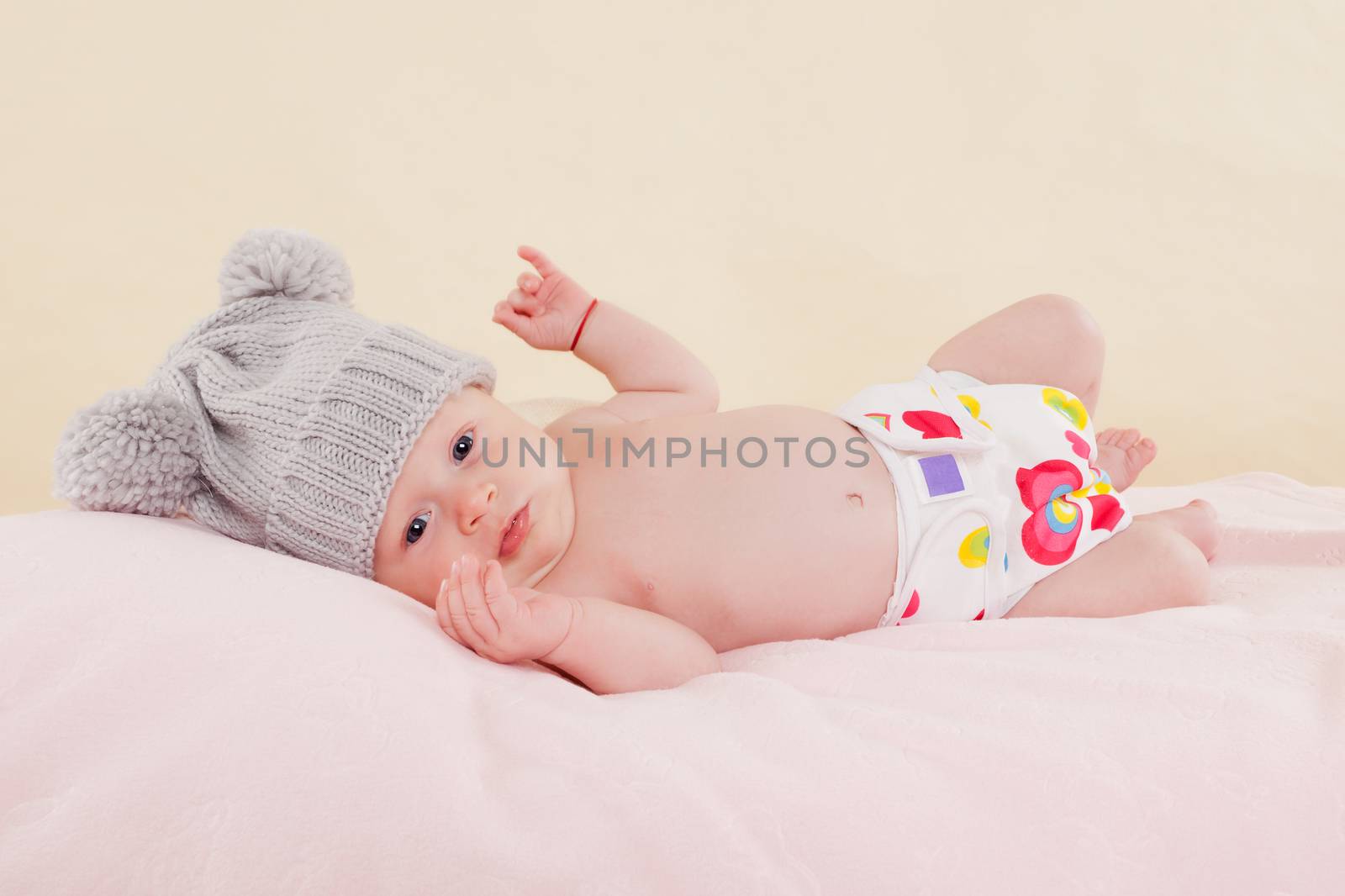 Cute baby girl with grey hat and diaper lying on blanket and looking into the camera. Beautiful newborn.
