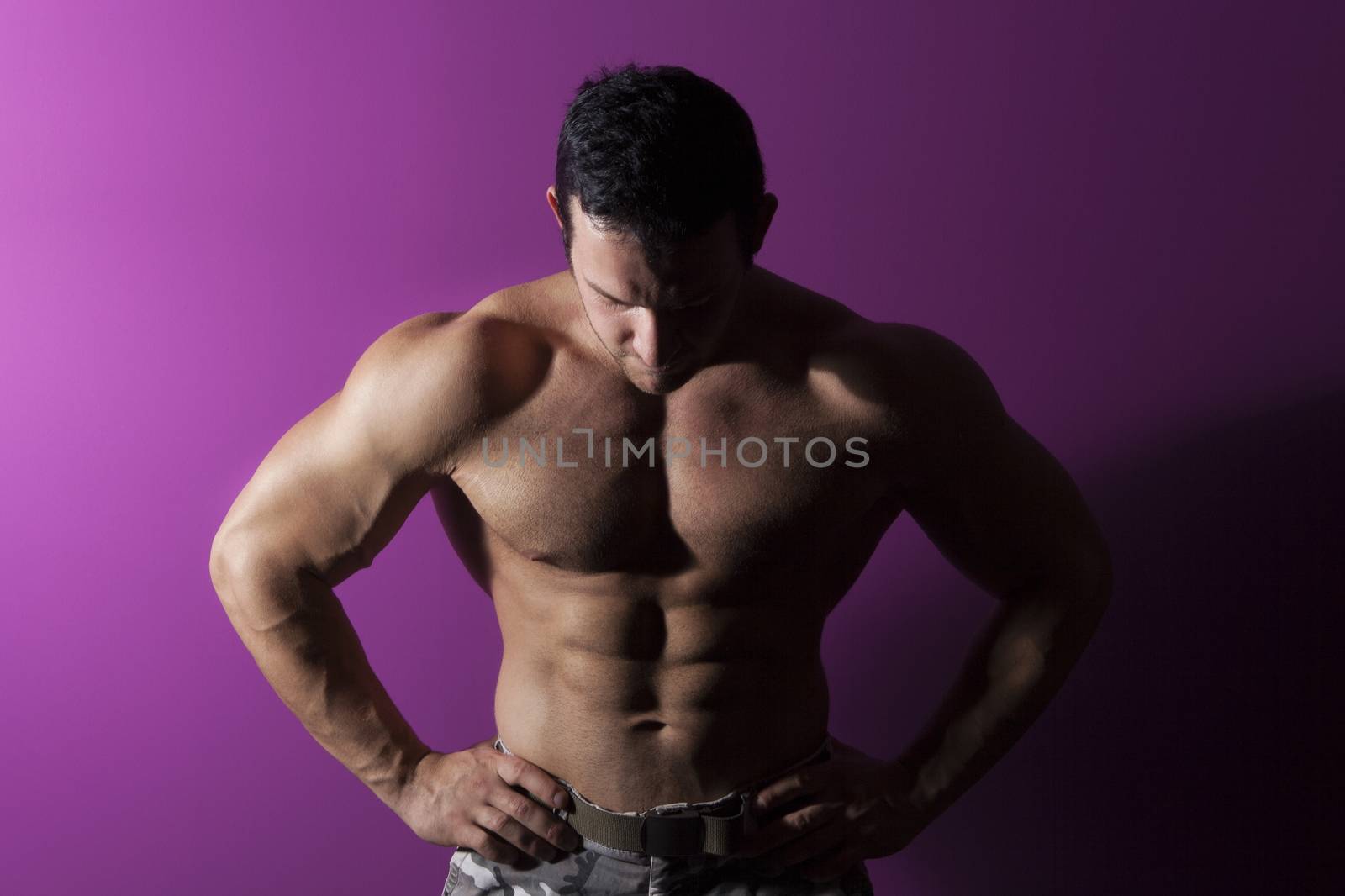 Sexy muscular bodybuilder isolated on purple background. Muscle and fitness fine art portrait.