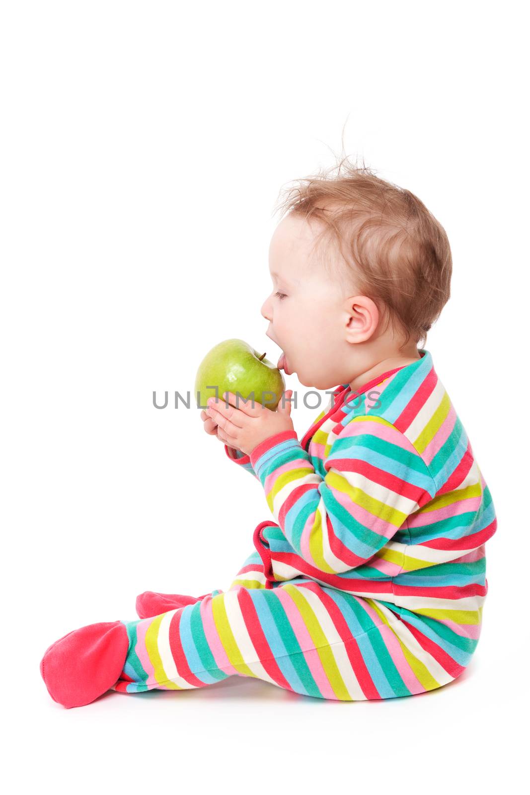 10 month old baby sitting and eating green apple isolated on white background. First teeth concept.