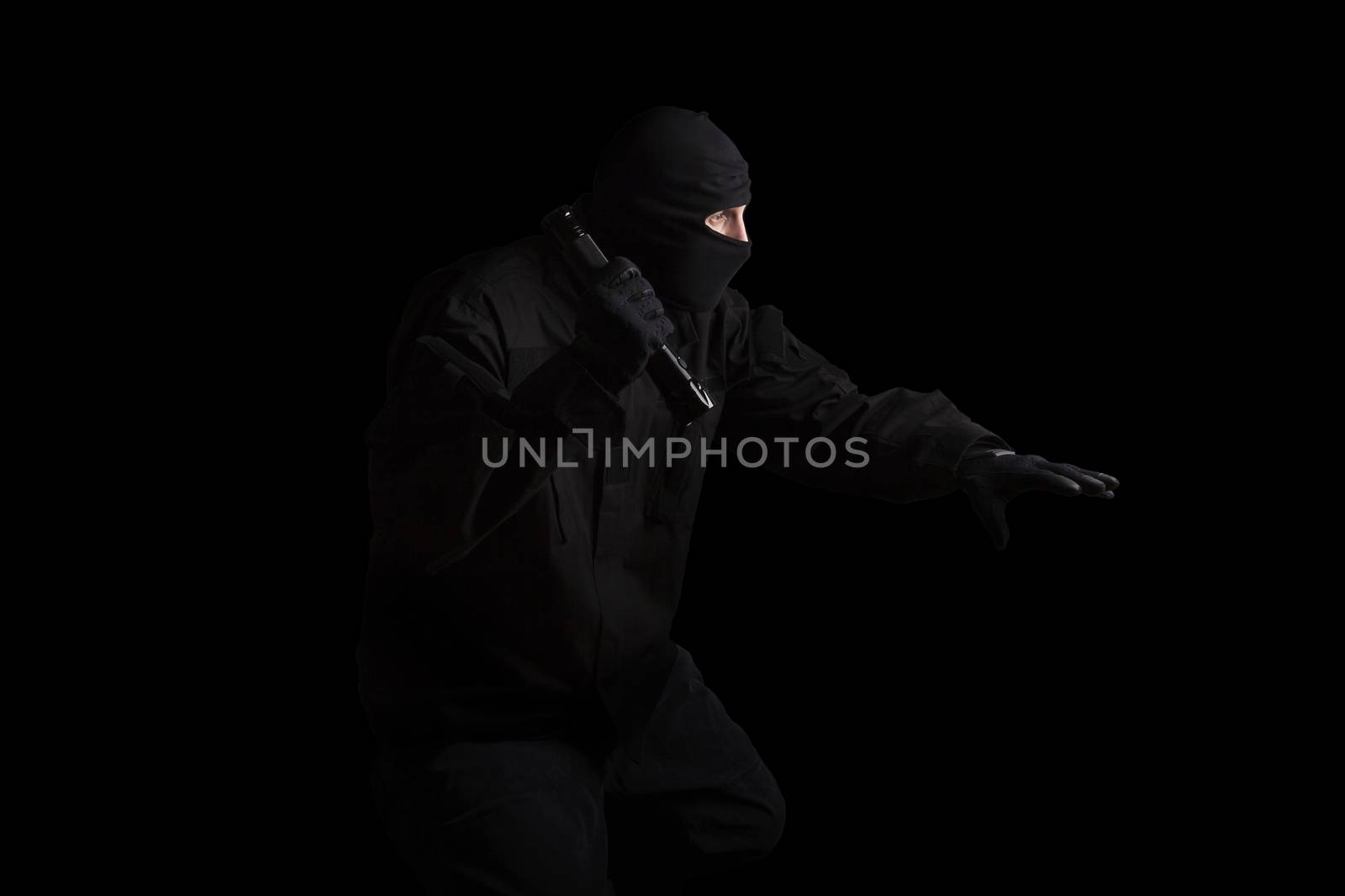 Man in black mask and black cloth holding flashlight isolated on black background. Dangerous criminal committing crime.