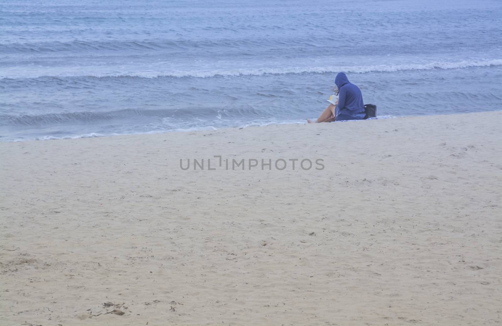 Beach reading. Young woman sitting on a sandy and empty beach reading a book. Mallorca, Balearic islands, Spain.