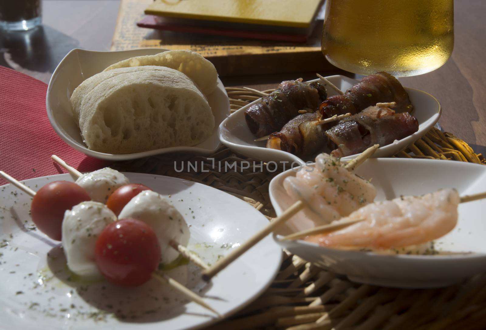 Bacon shrimp tapas plates. Plates with varied tapas: tomatoes, mozzarella, bread, shrimp, dates with bacon and a glass of beer on a restaurant. Mallorca, Balearic islands, Spain.