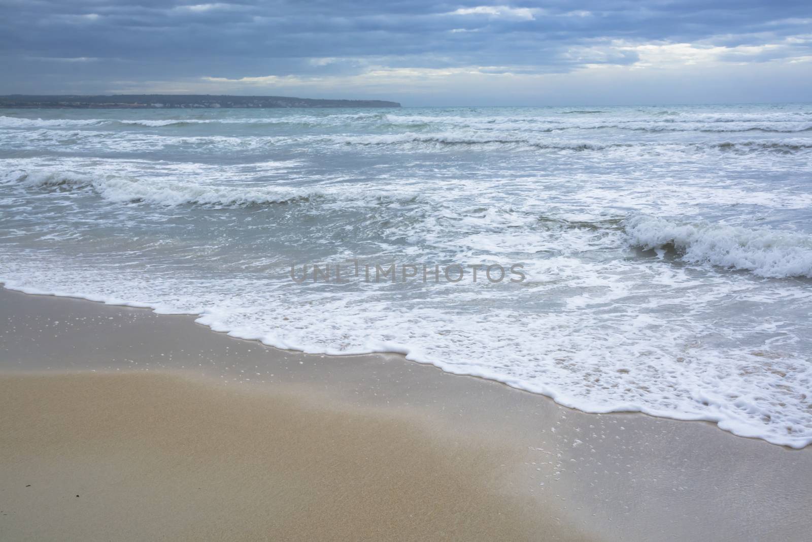 Mediterranean blues in autumn. Sandy beach and storm waves in November, Mallorca, Balearic islands, Spain.