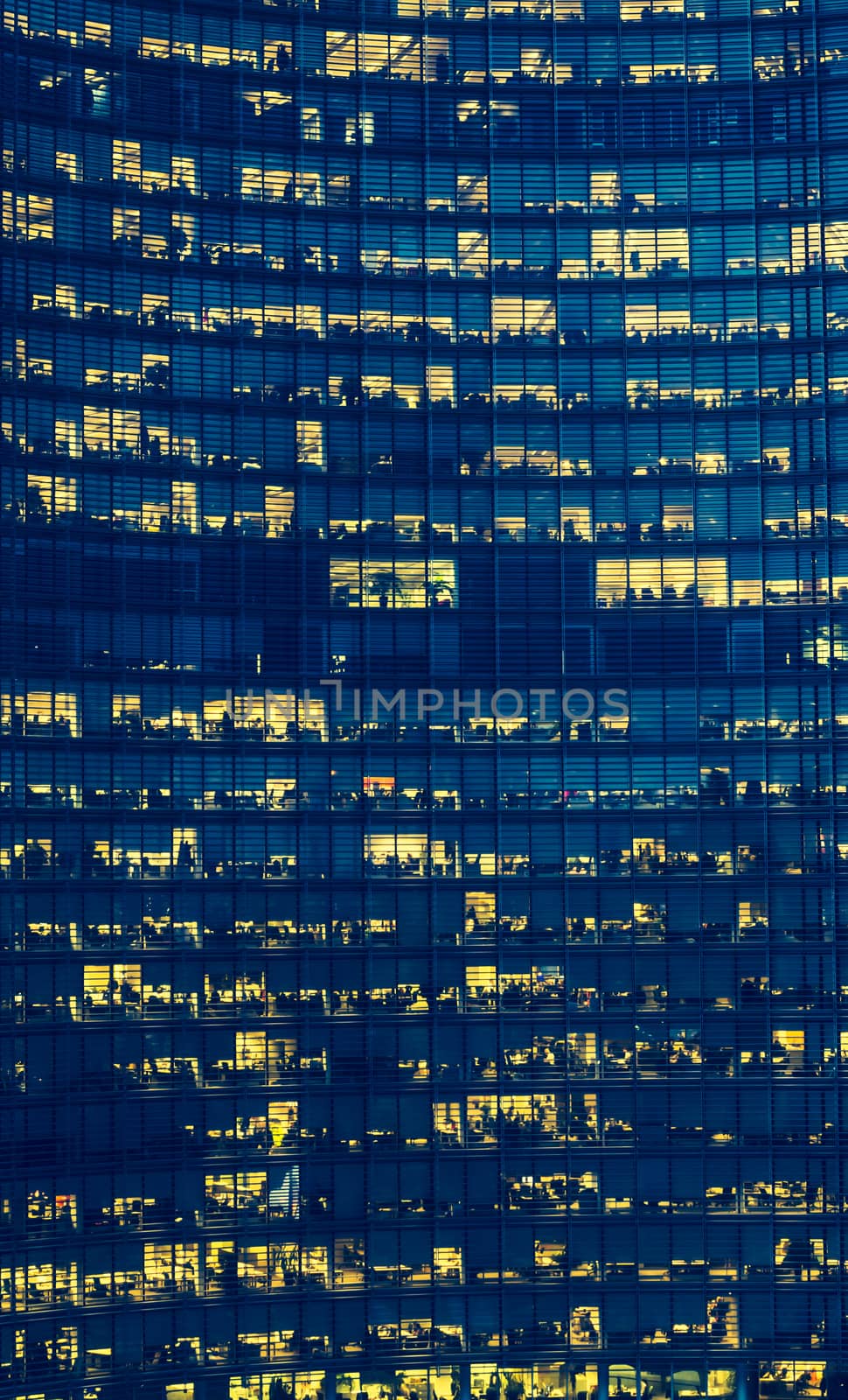 High Rise Office Building with many floors and visible but anonymous people at dusk.