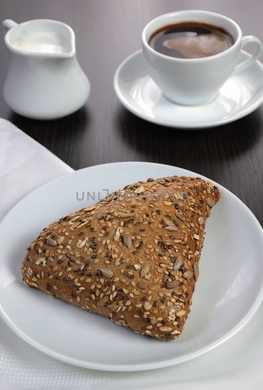 Bun with cereals with a cup of coffee and milk on the table