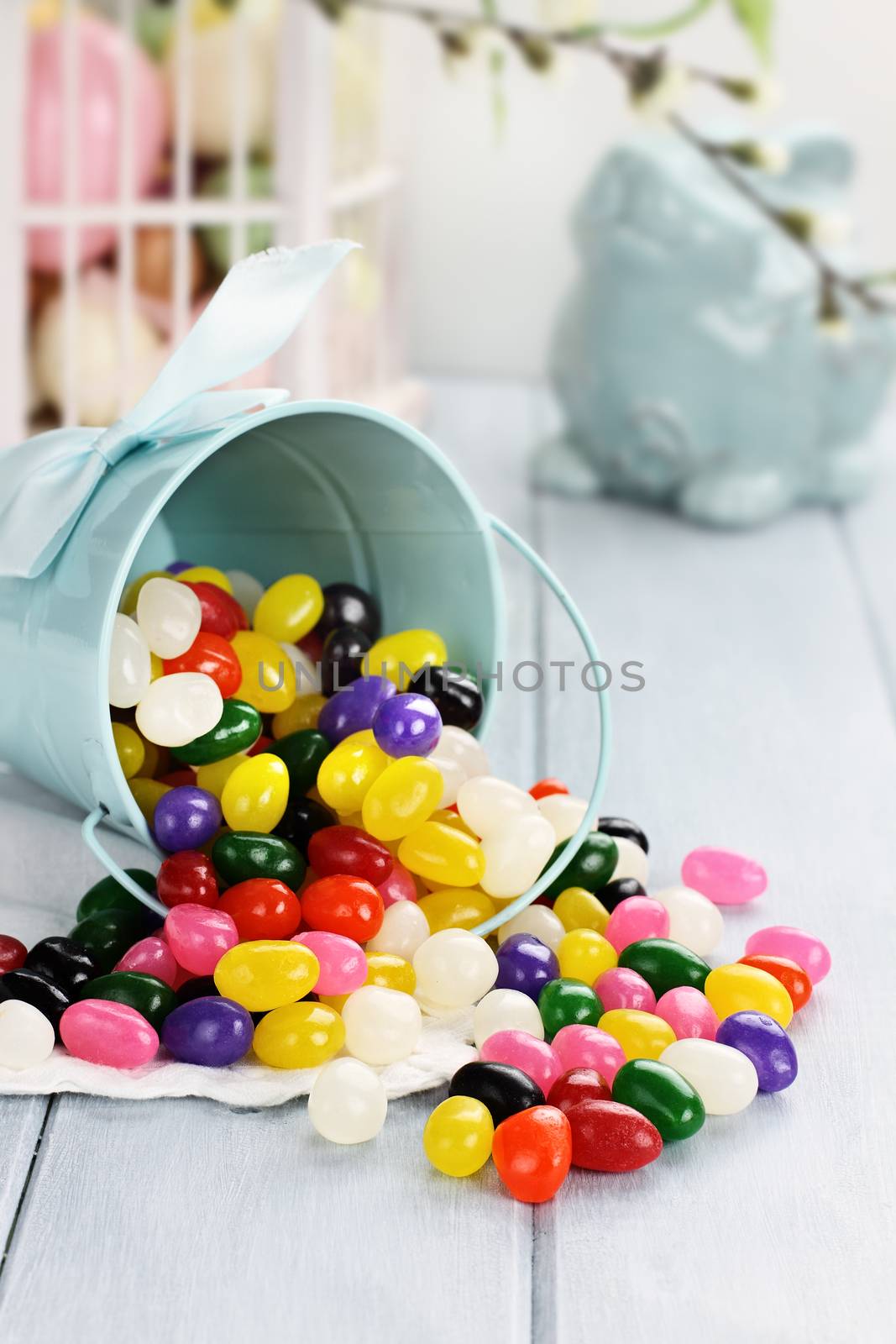 A blue tin bucket tipped over, spilling jelly beans onto a table. Shallow depth of field.