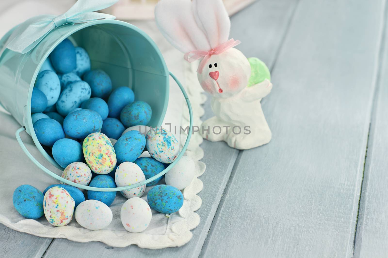 A blue tin bucket tipped over, spilling Easter candy eggs onto a table. Shallow depth of field.