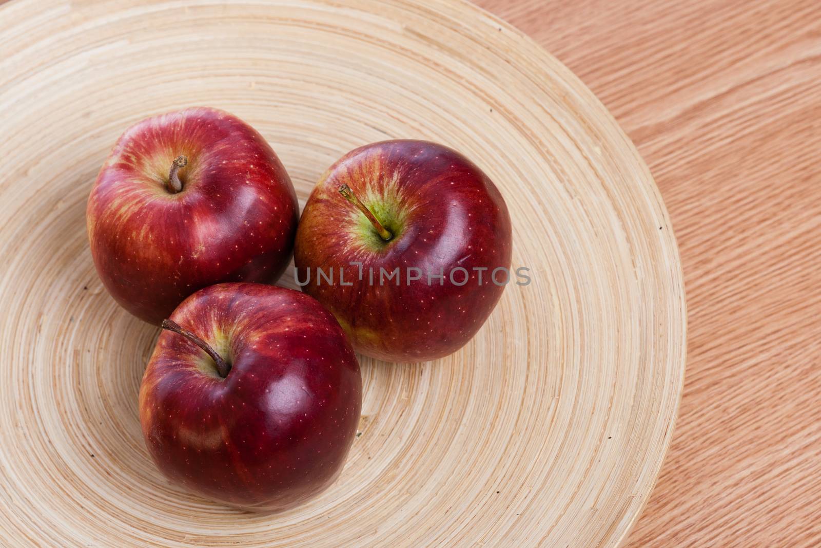 three red apples on a wooden plate