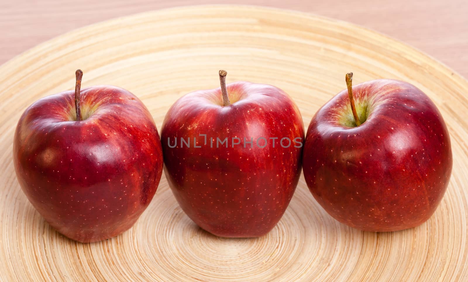 three red apples on a wooden plate