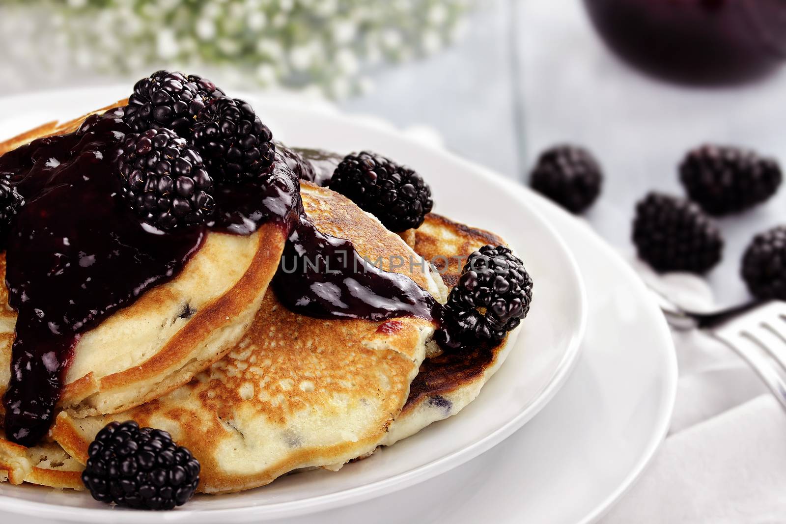 Delicious golden pancakes with fresh blackberries and blackberry jam. Extreme shallow depth of field.