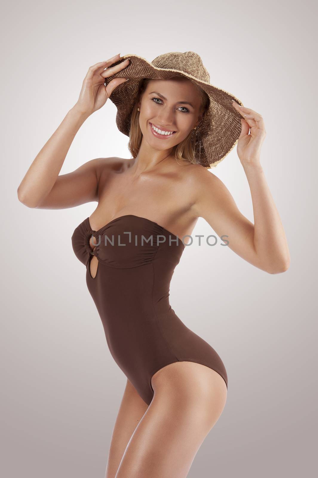 young beautiful smiling woman in brown swim suit and summer hat looking in camera