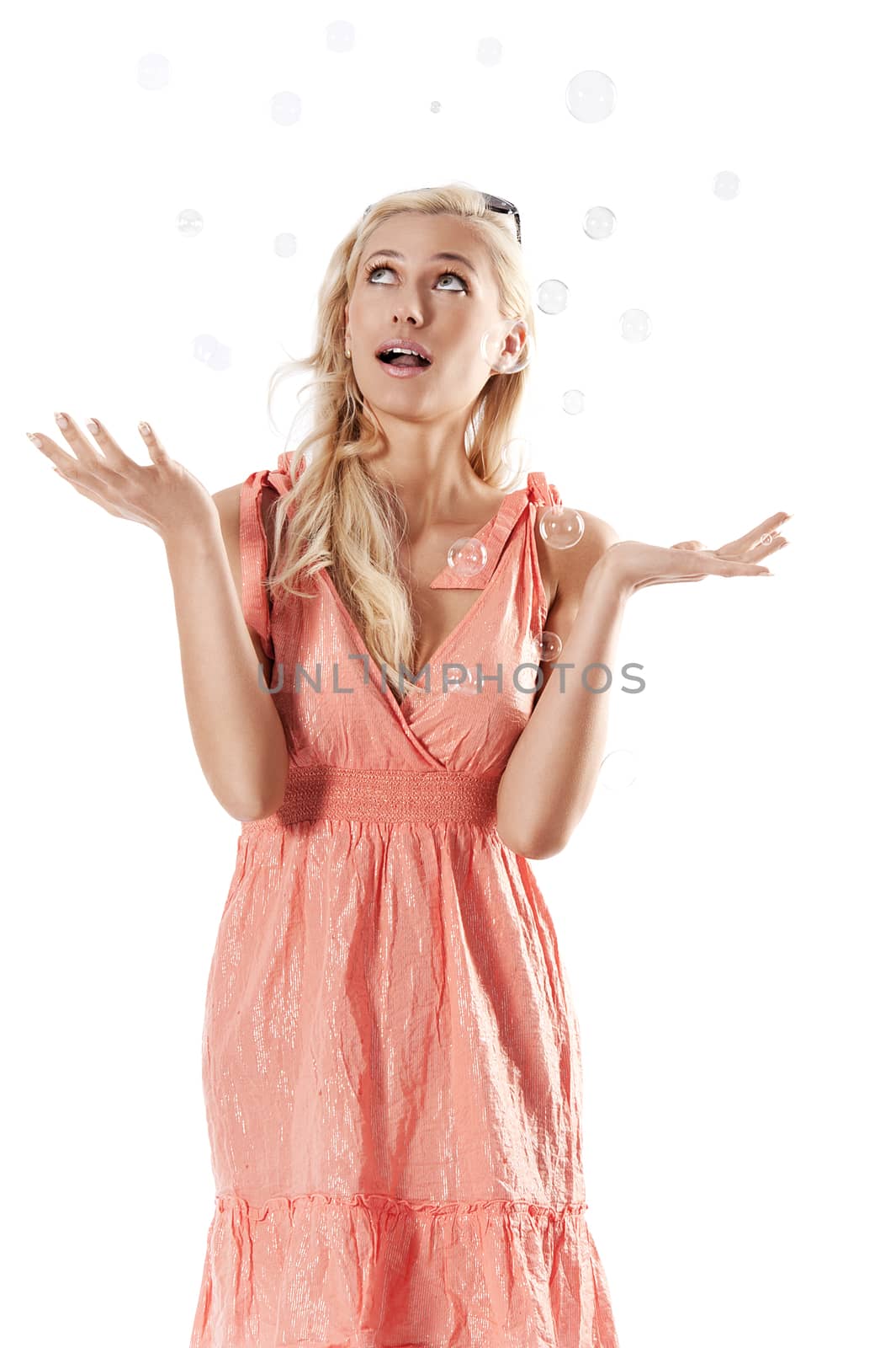 pretty young blond woman wearing a summer orange dress standing against white background looking towards the soap bubbles