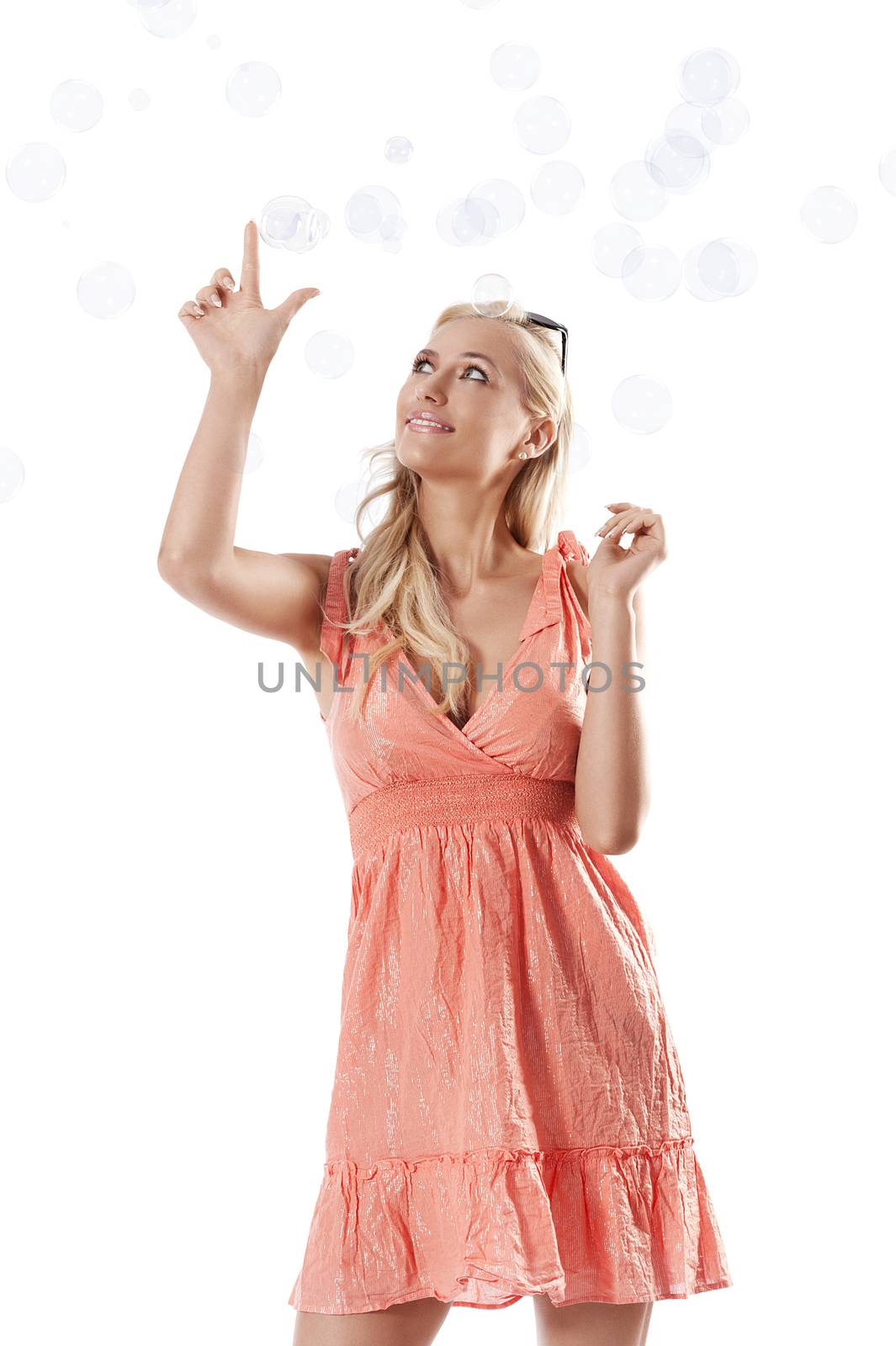 pretty young blond woman wearing a summer orange dress standing against white background playing with some soap bubbles