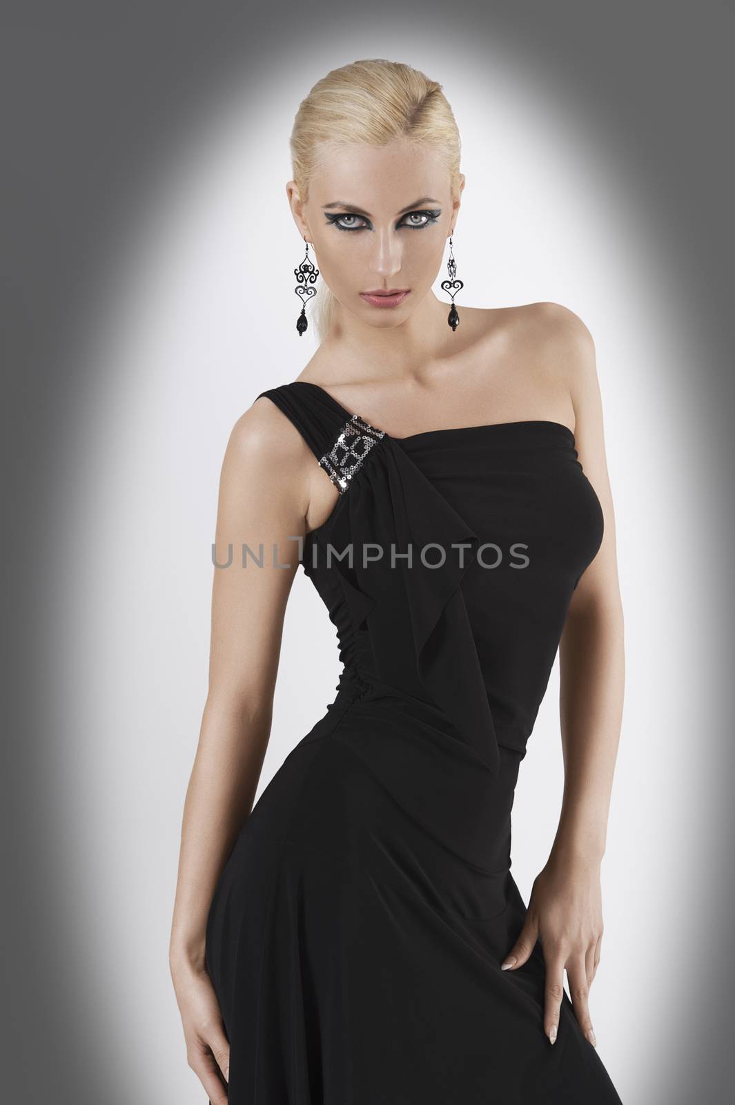blond attractive young woaman in black dress and black earring looking in camera with strong and sexy eyes and wit sexy pose looking towards the camera