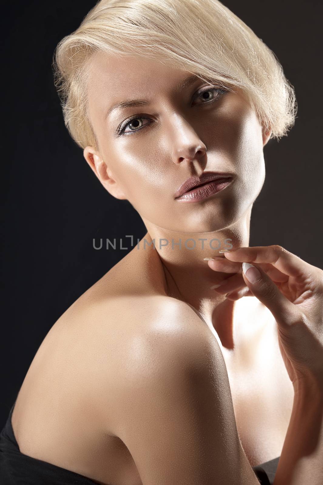 Emotive dark portrait of a blond young woman with an up do and naked shoulder on black background