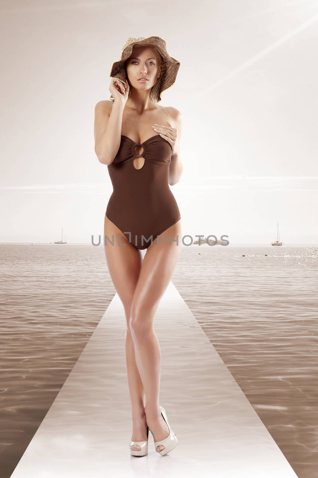 stunning young woman wearing a brown swimsuit and a summer hat posing