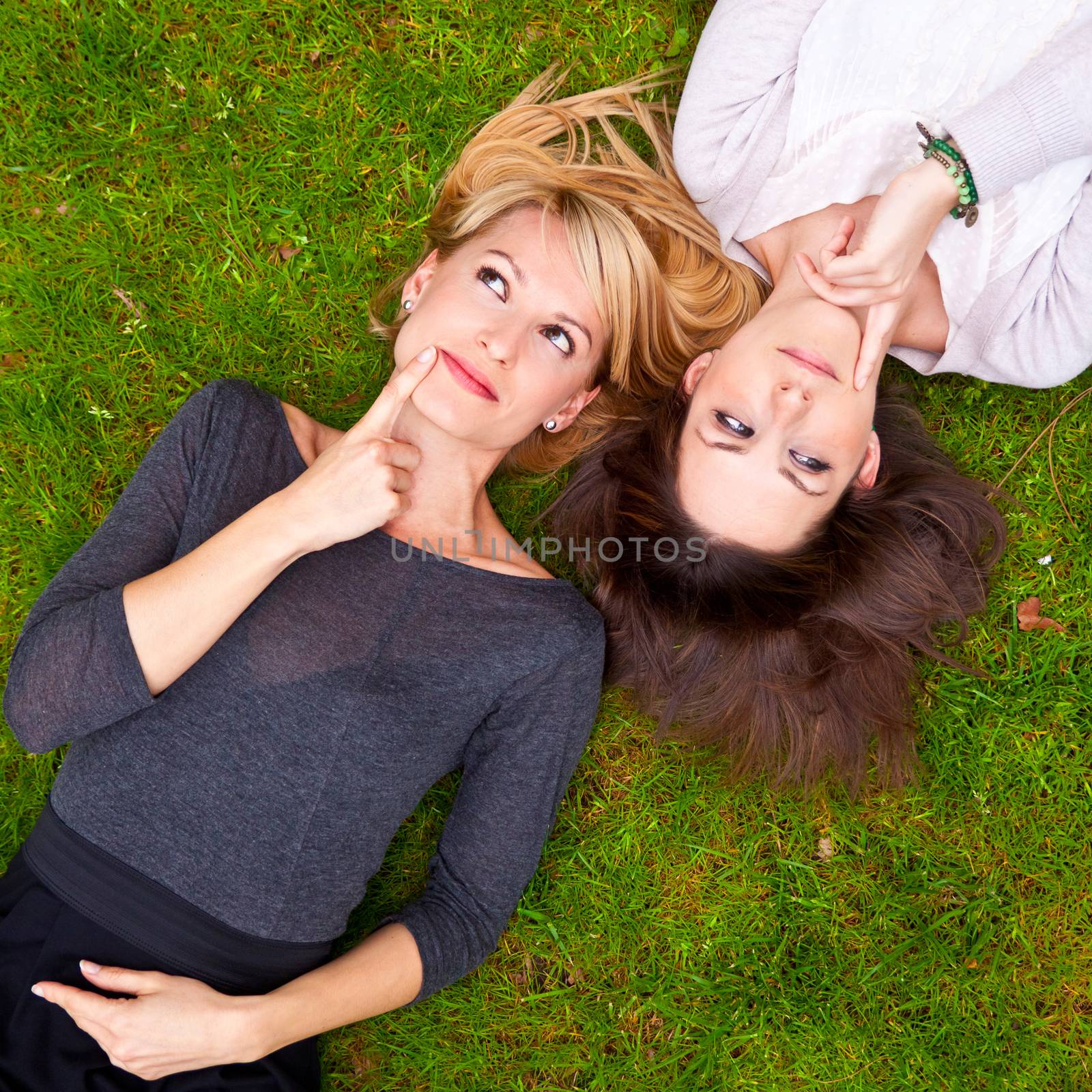 Two beautiful girls brainstorming in the grass.