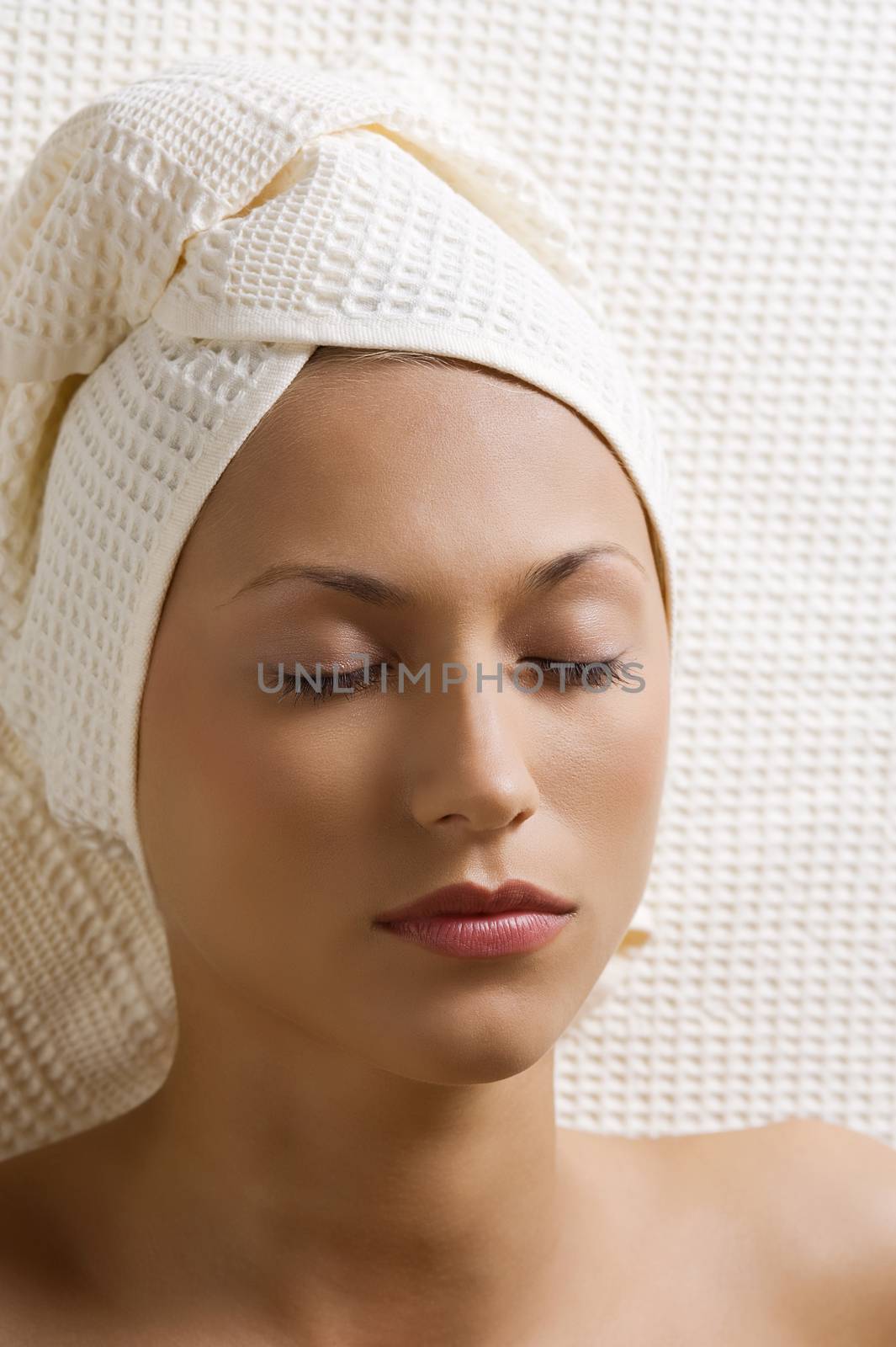 portrait of a young woman with bath towels and closed eyes resting in spa