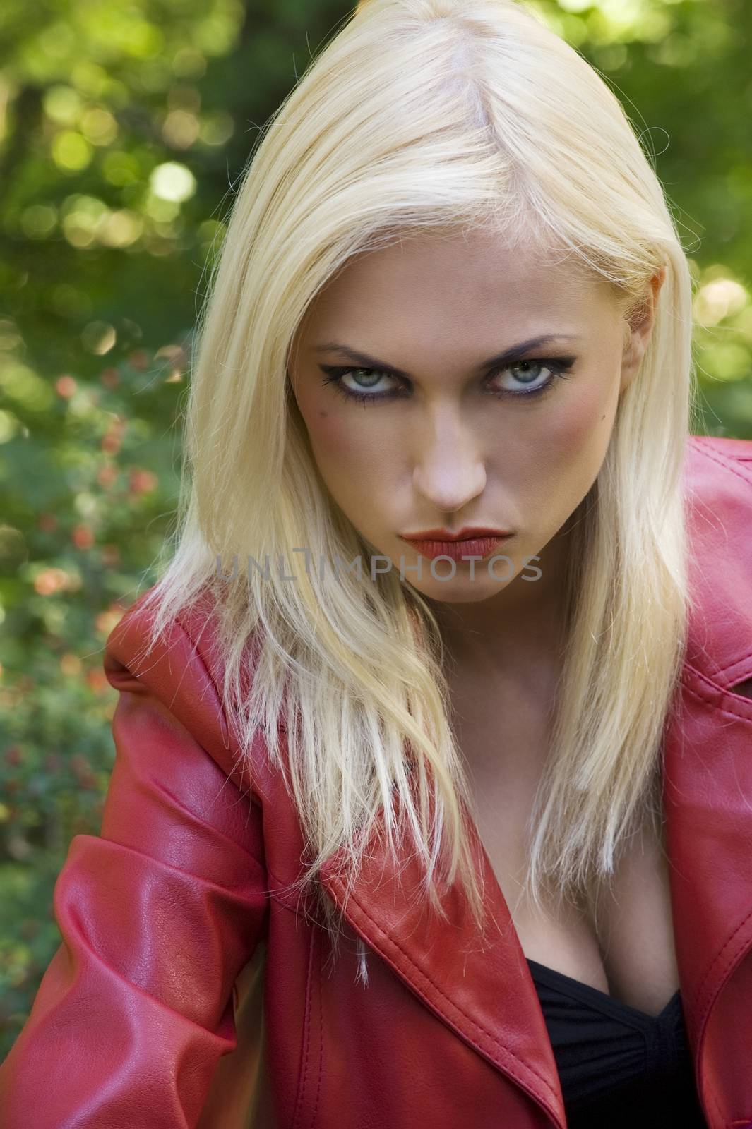 Closeup dark portrait of a sensual blond girl with red coat in park looking anger