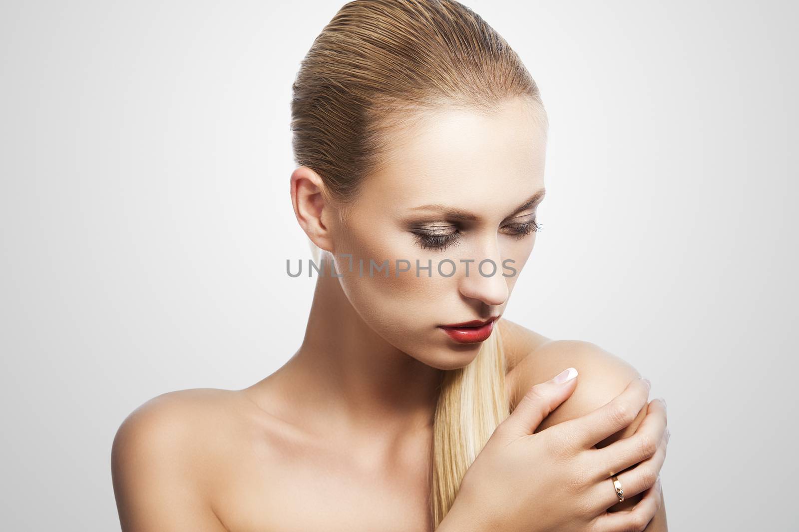 blond pretty woman in a beauty portrait with wet hair and a straight tail over shoulder. She looks down at left, the tail is over the left shoulder and she has a right hand on that.