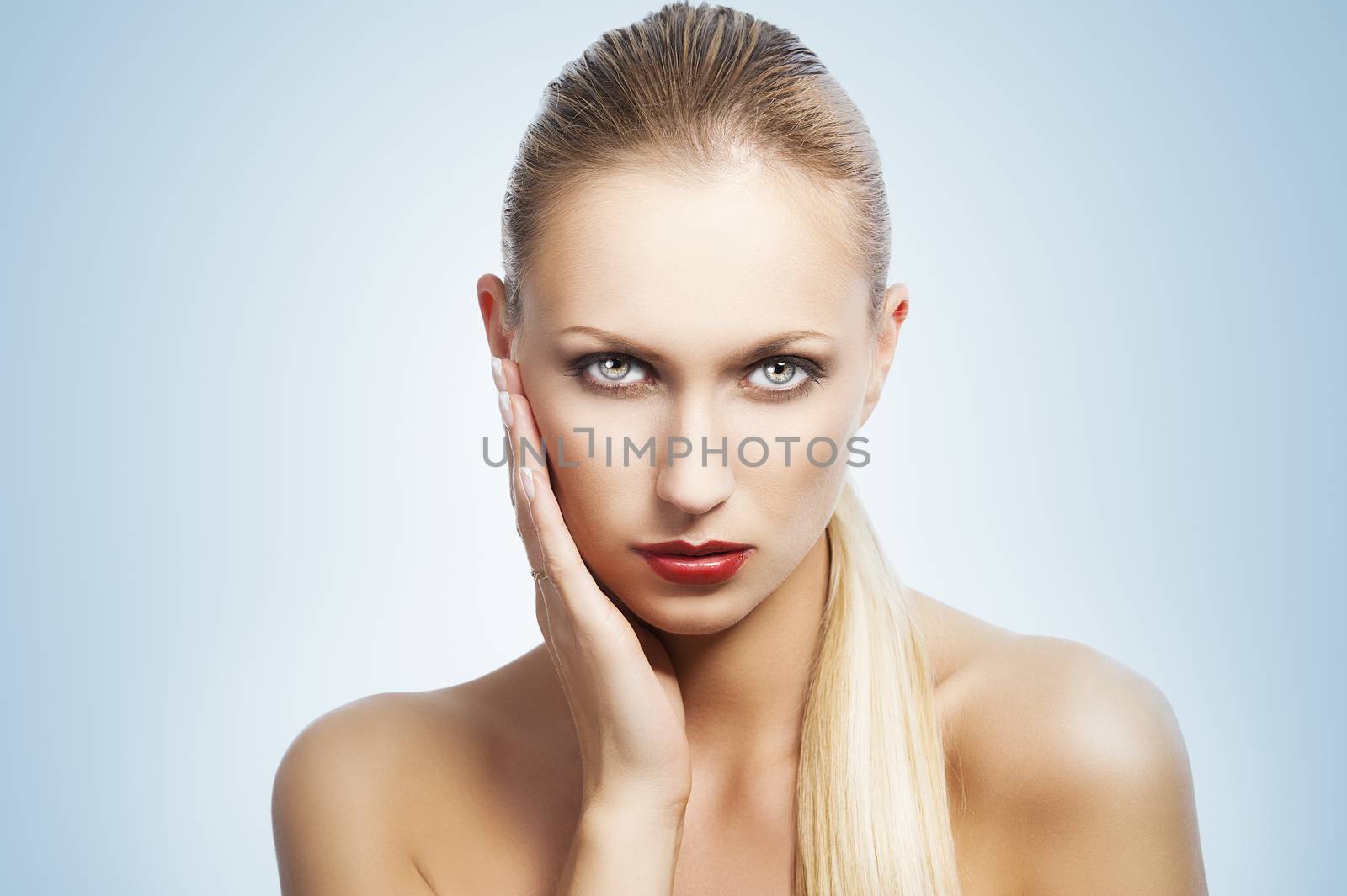 blond pretty woman in a beauty portrait with wet hair and a straight tail over shoulder. She looks in to the lens, the tail is over the left shoulder and she has a right hand near the face