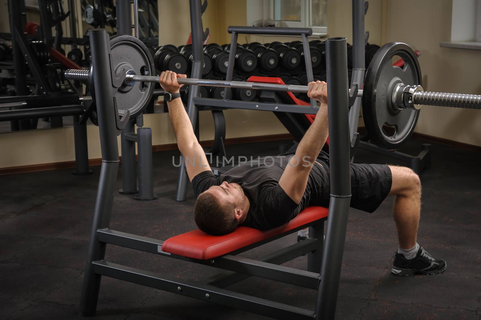 young man doing bench press workout in gym by starush