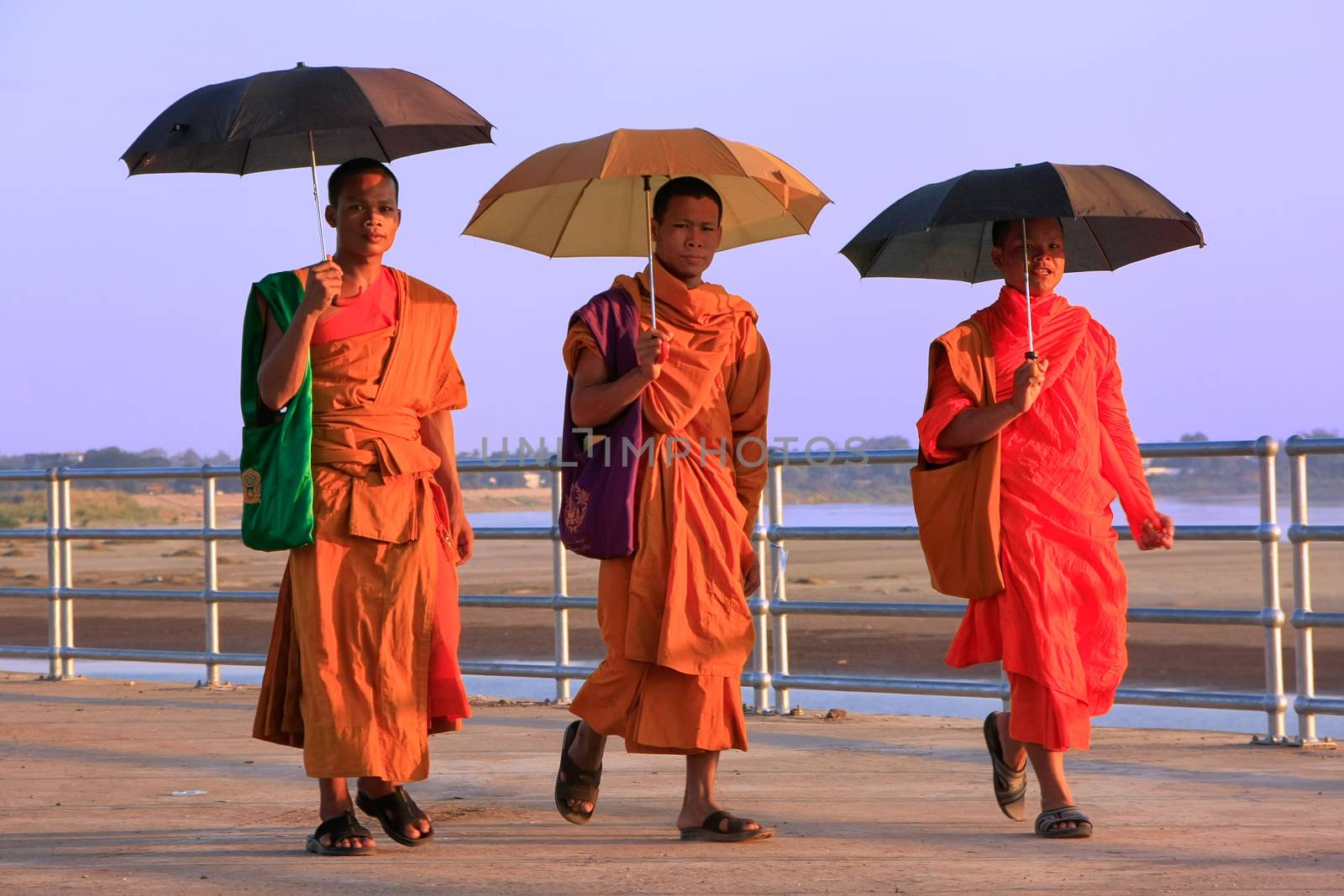 Monks with umbrellas walking near Mekong river, Vientiane, Laos by donya_nedomam