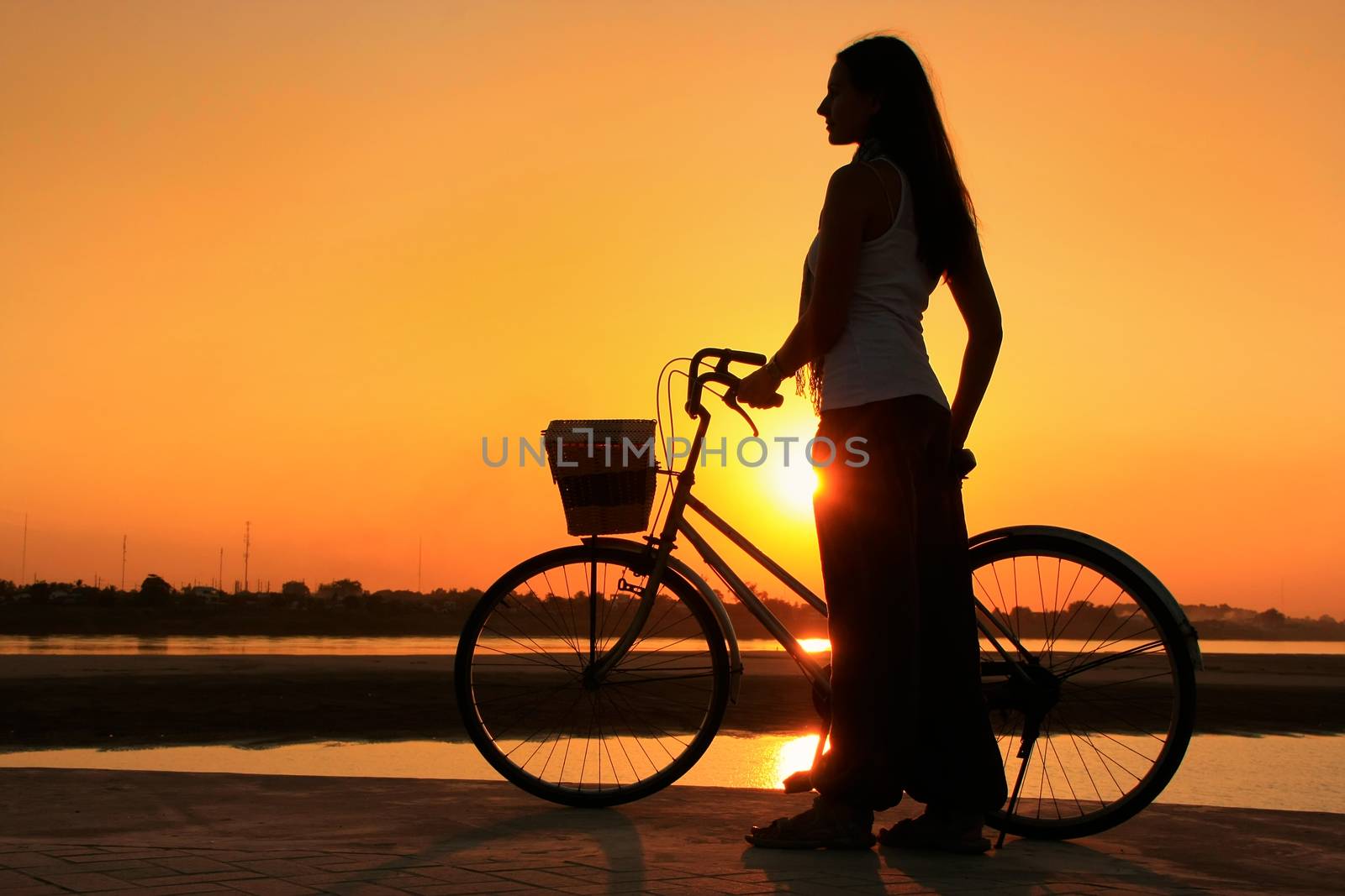 Silhouetted woman with bicycle at Mekong river waterfront at sunset, Vientiane, Laos, Southeast Asia