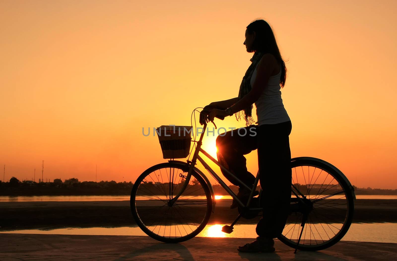 Silhouetted woman with bicycle at Mekong river waterfront at sun by donya_nedomam