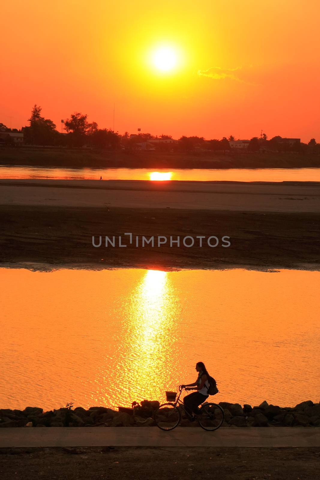 Silhouetted woman riding at Mekong river waterfront at sunset, V by donya_nedomam