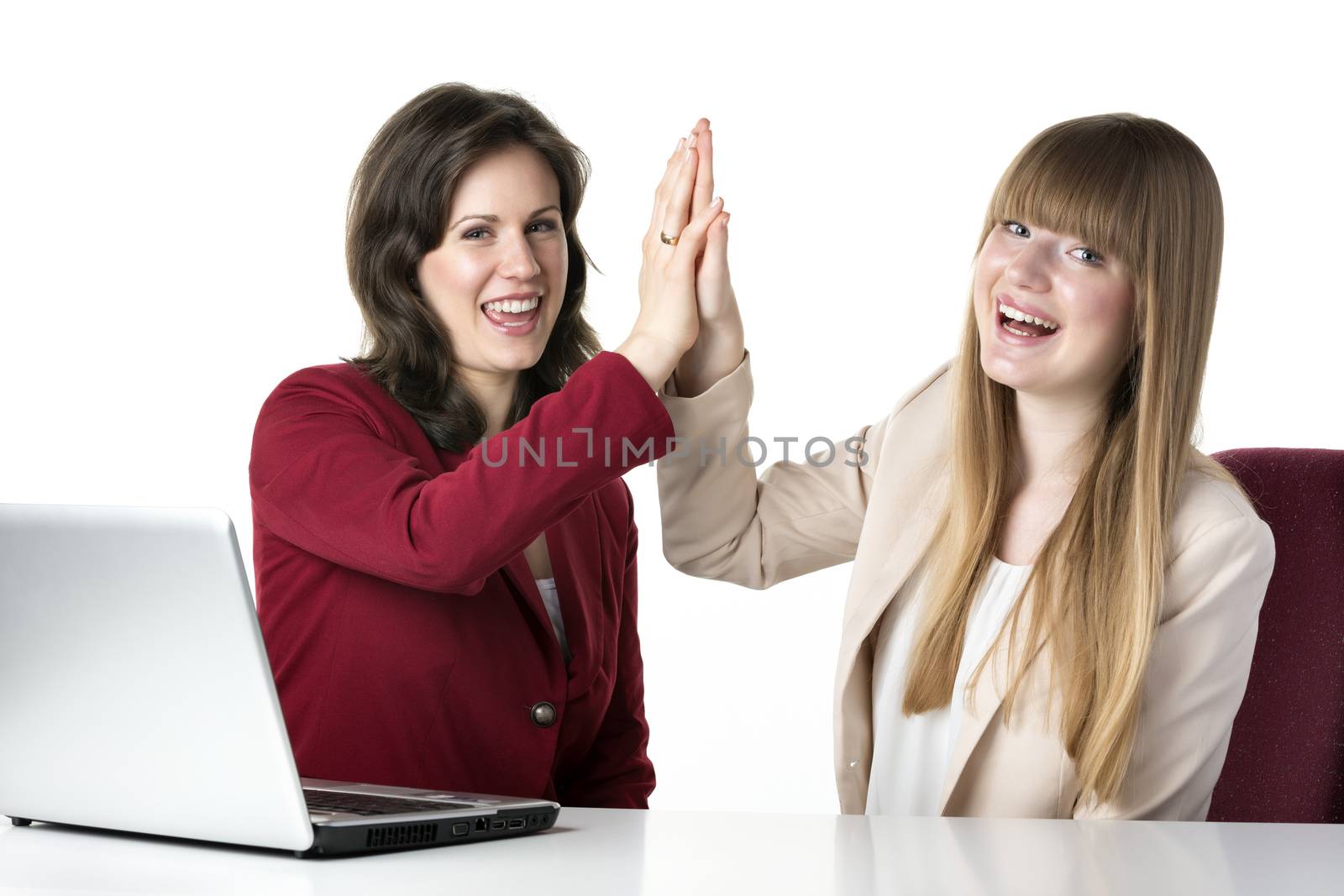 Two happy women blonde and brunette, sitting together in front of a laptop