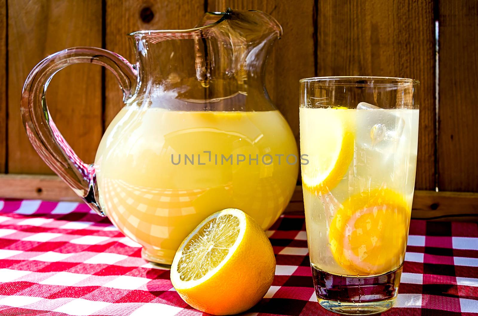 Lemonade and pitcher with sliced lemons on red gingham table cloth. 
