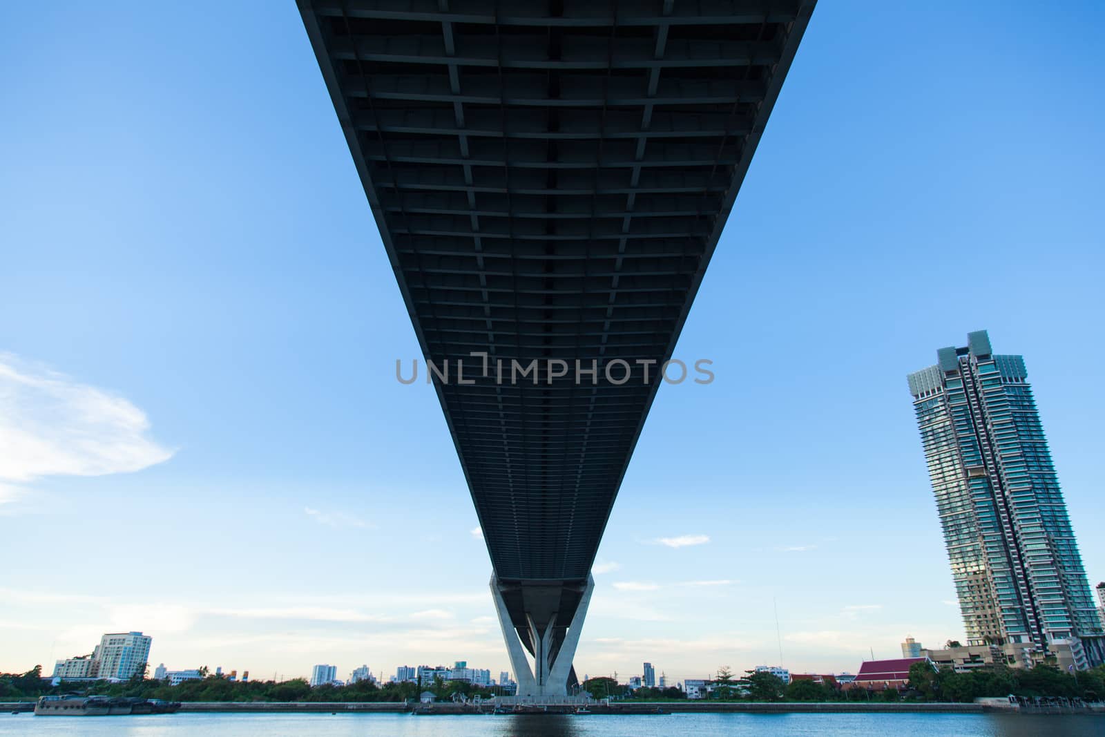 Bridge over a large river. Of surface reflects blue sky. Opposite side of the building in the city.