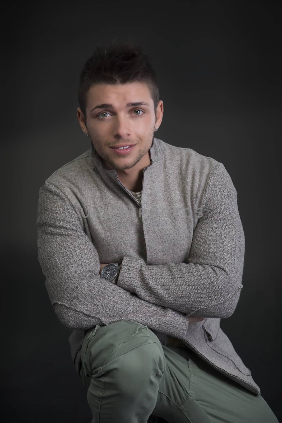 Attractive young man with sweater, sitting on the floor on dark background