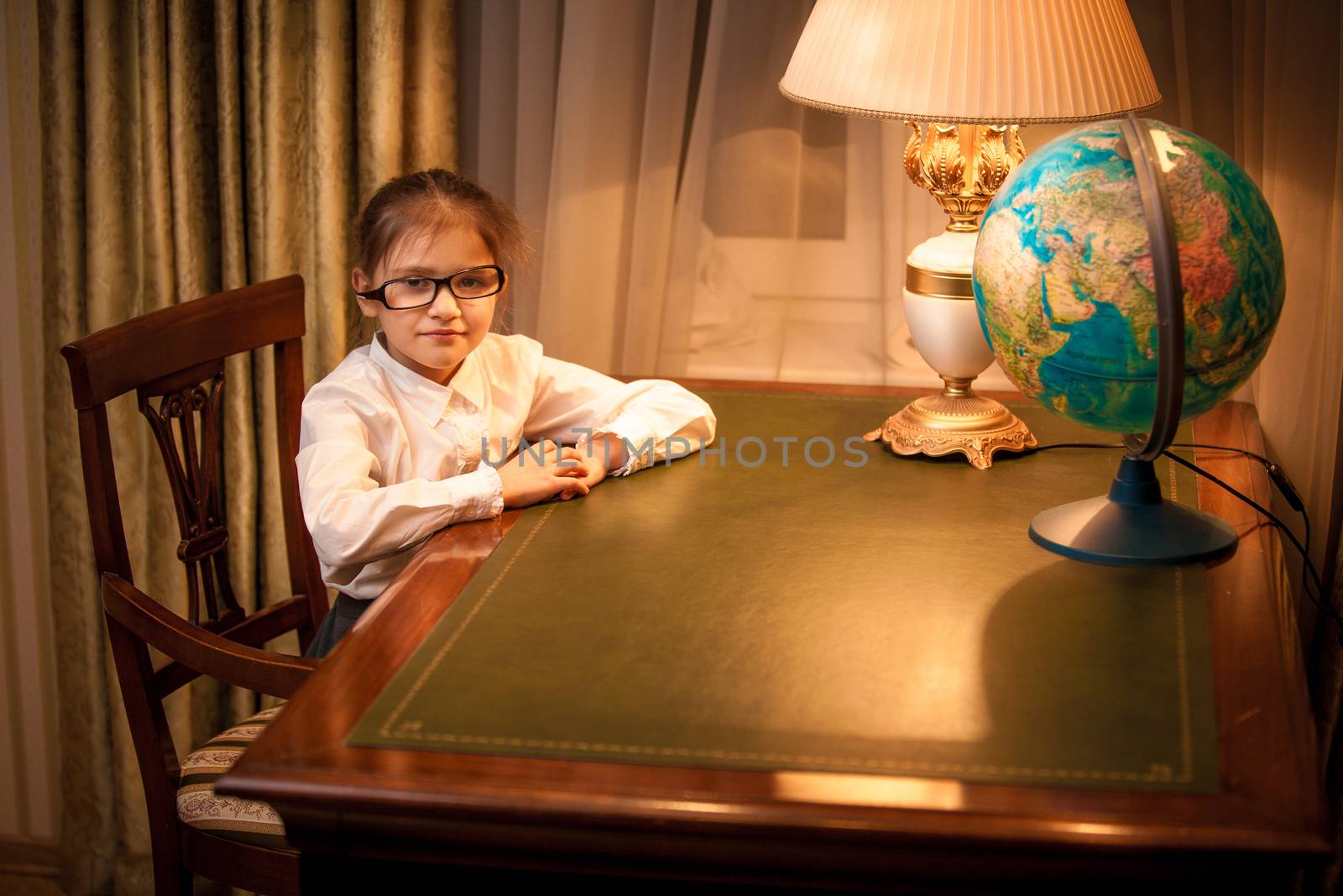 Little girl in eyeglasses sitting behind desk by Kryzhov