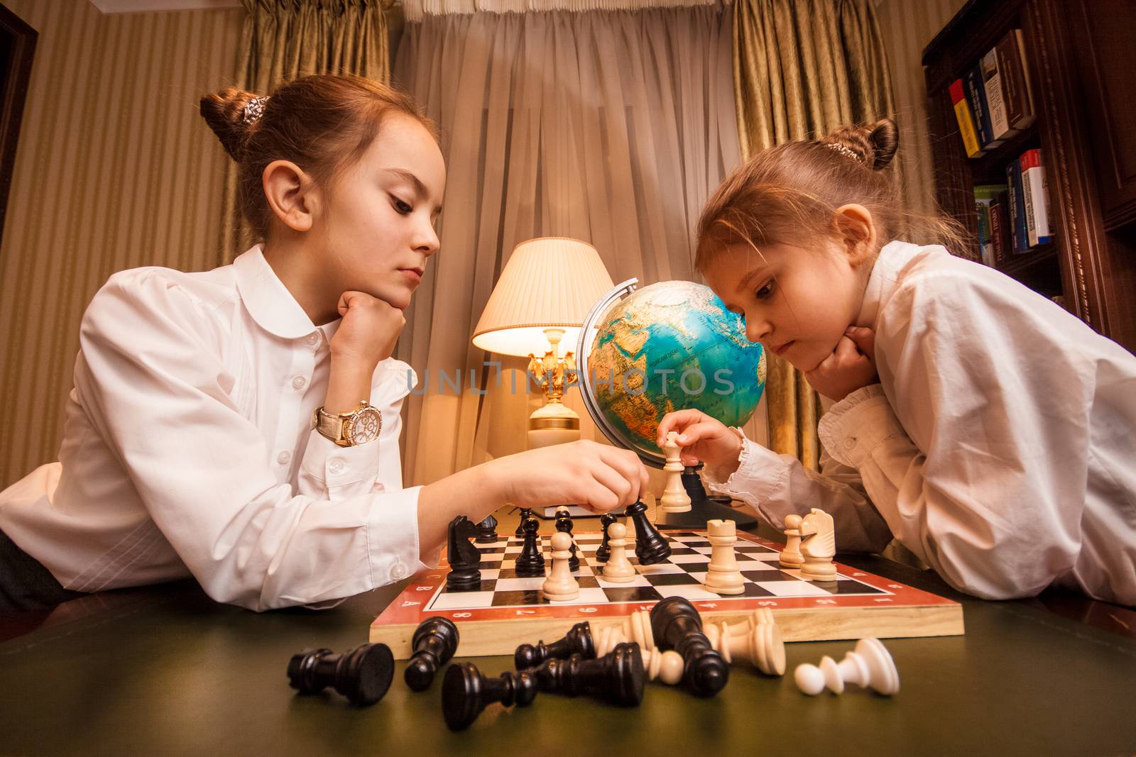Portrait of two little sisters playing chess