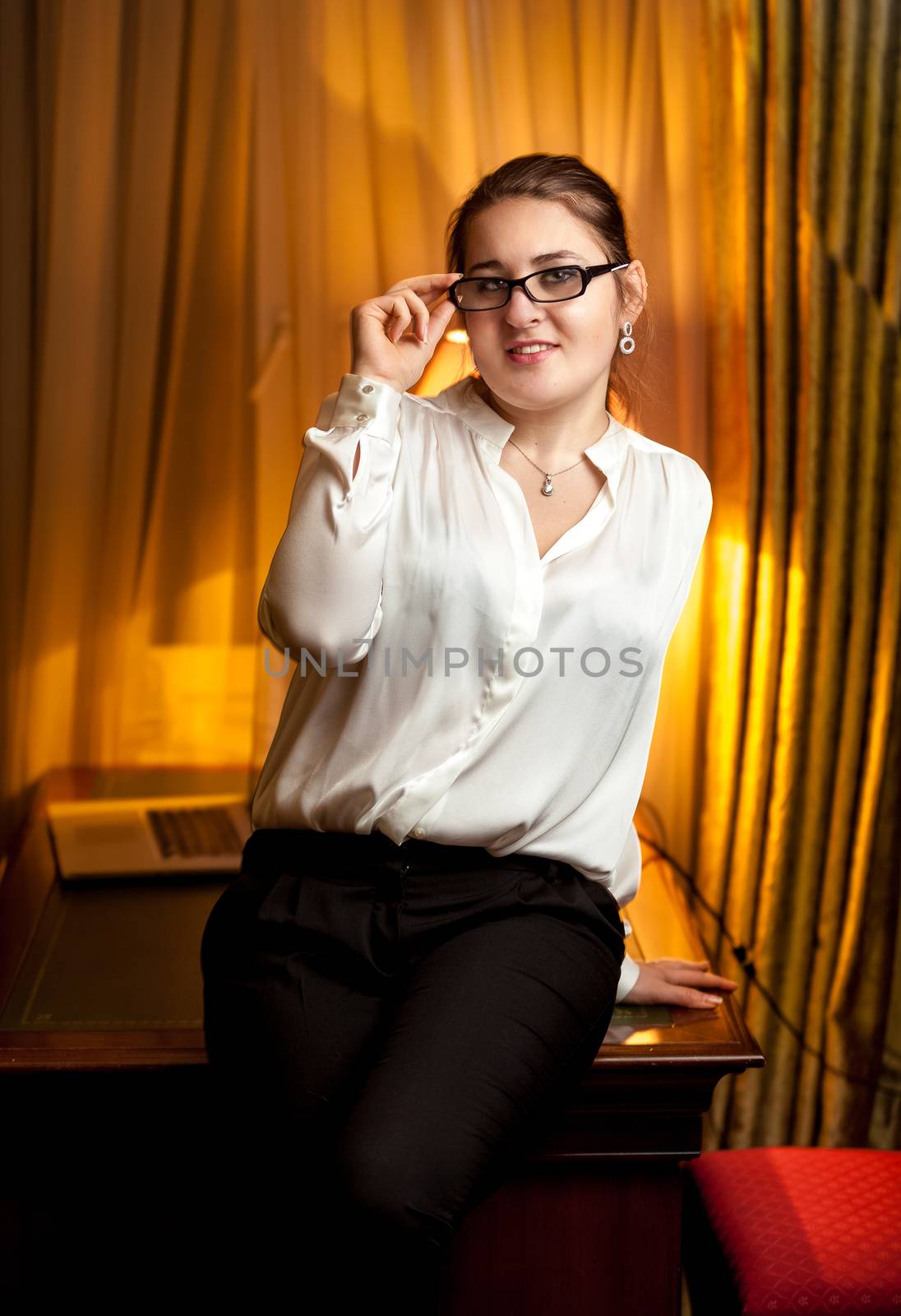 Businesswoman in eyeglasses and white blouse sitting on table