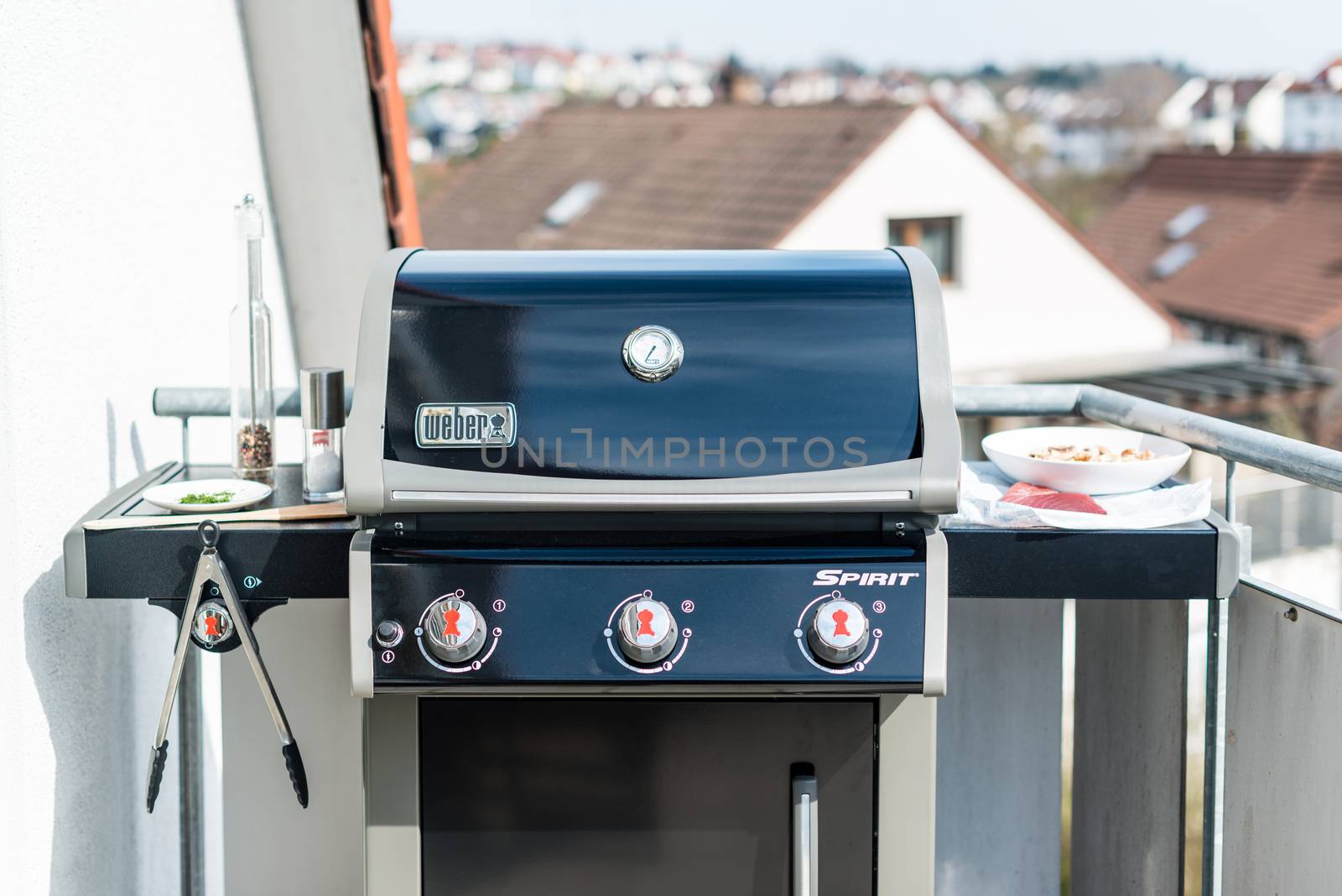 NEUHAUSEN, GERMANY - MARCH 27, 2014: A brand new Weber BBQ Gas Grill Spirit S320 black edition (model 2014) is waiting for its first use on March 27, 2014 in Neuhausen (near Stuttgart), Germany. The lid of the grill is closed, some utensils like BBQ tongs, a spatula, pepper and salt plus some herbs are placed on one of its sideboards. The other one is carrying a red tuna steak and some mushrooms on a plate.