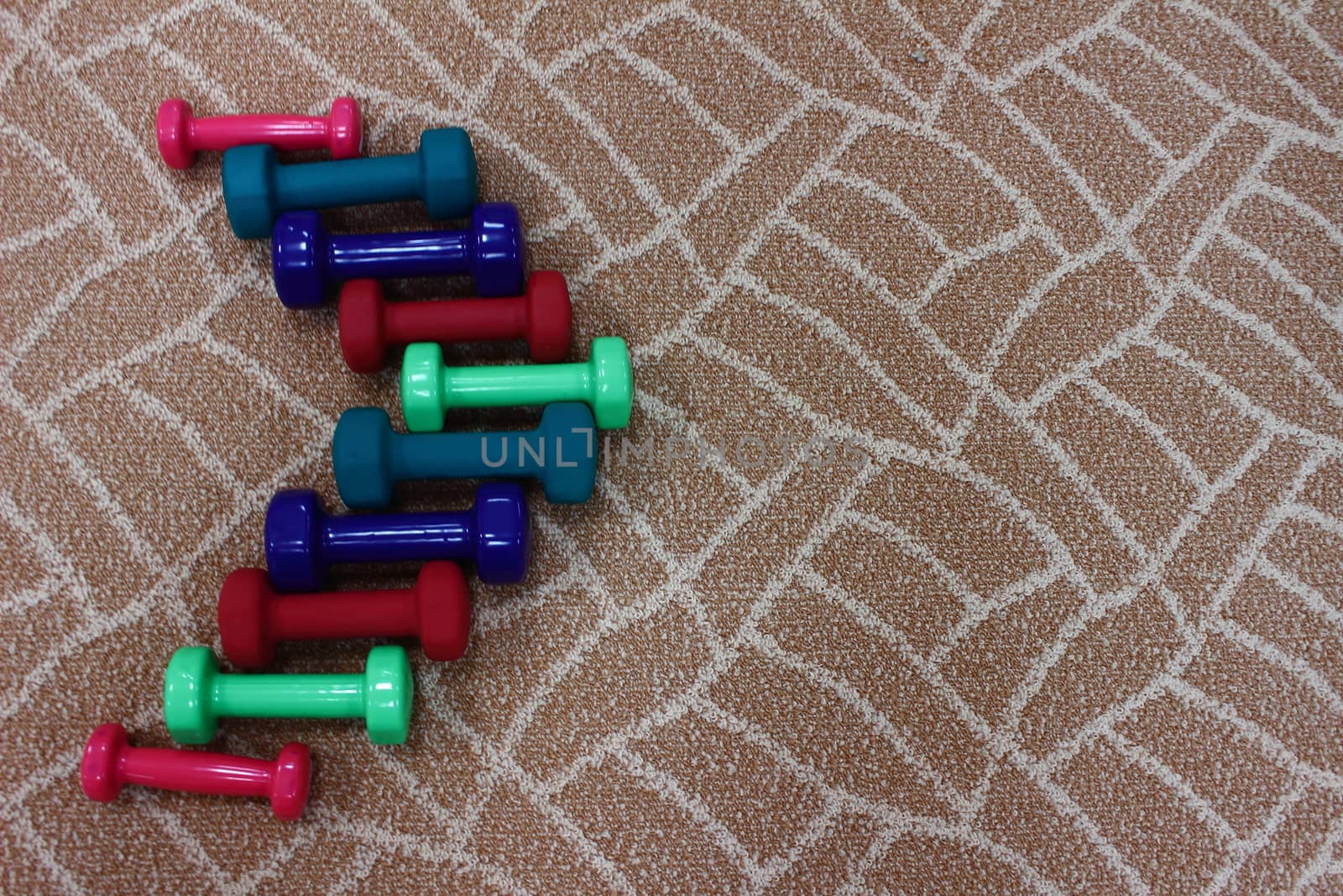 Colorful dumbbells lined up in an arrow pointer on the carpet in the gym