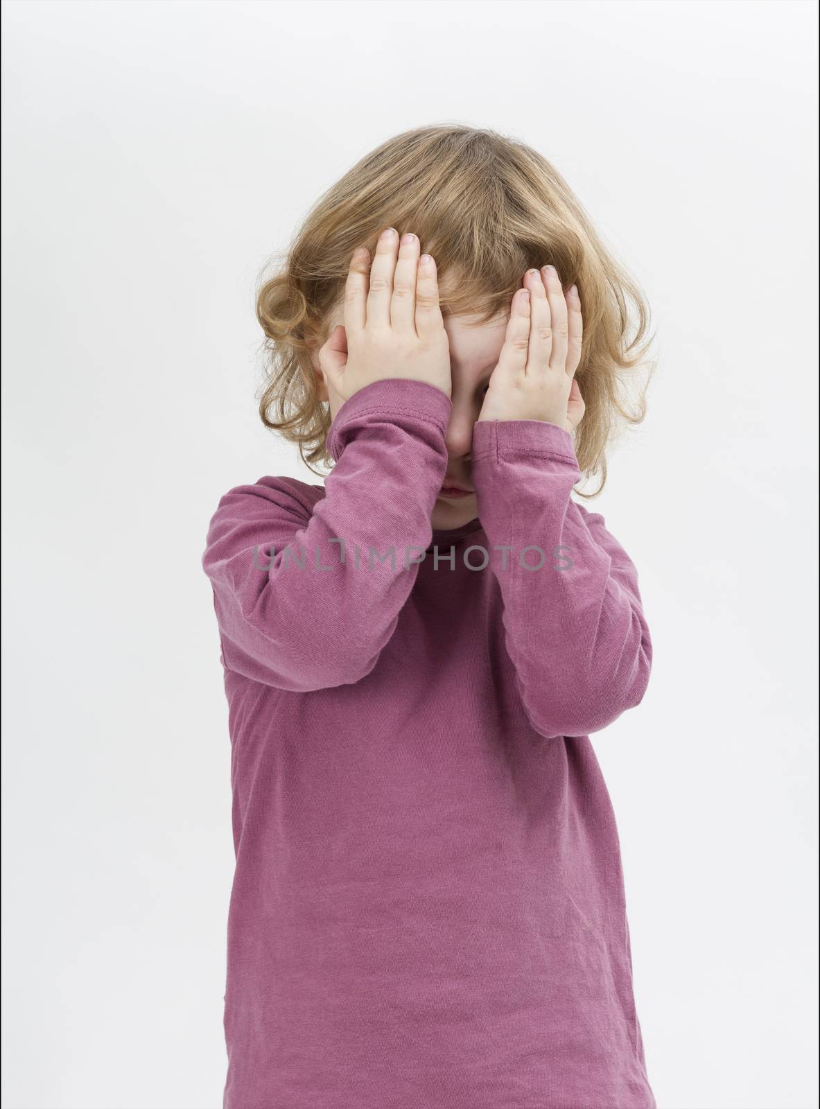 child covering eyes with hands. studio shot in grey background