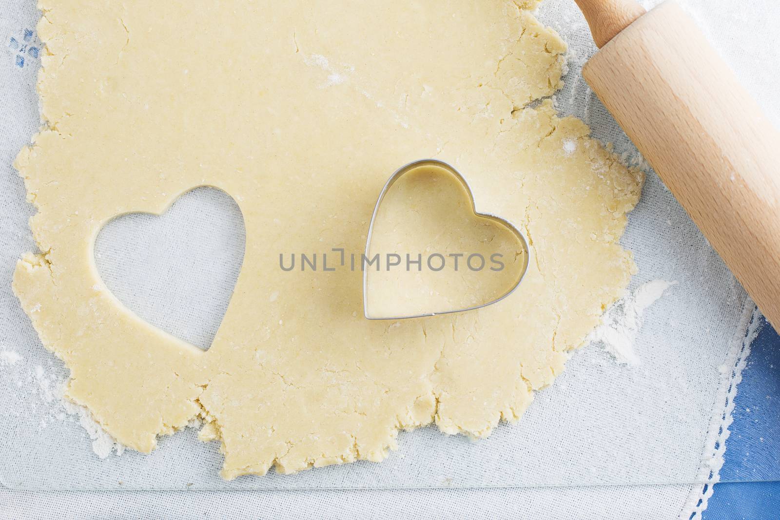 Heart shaped cookie cut out of cookie dough with cutter and rolling pin
